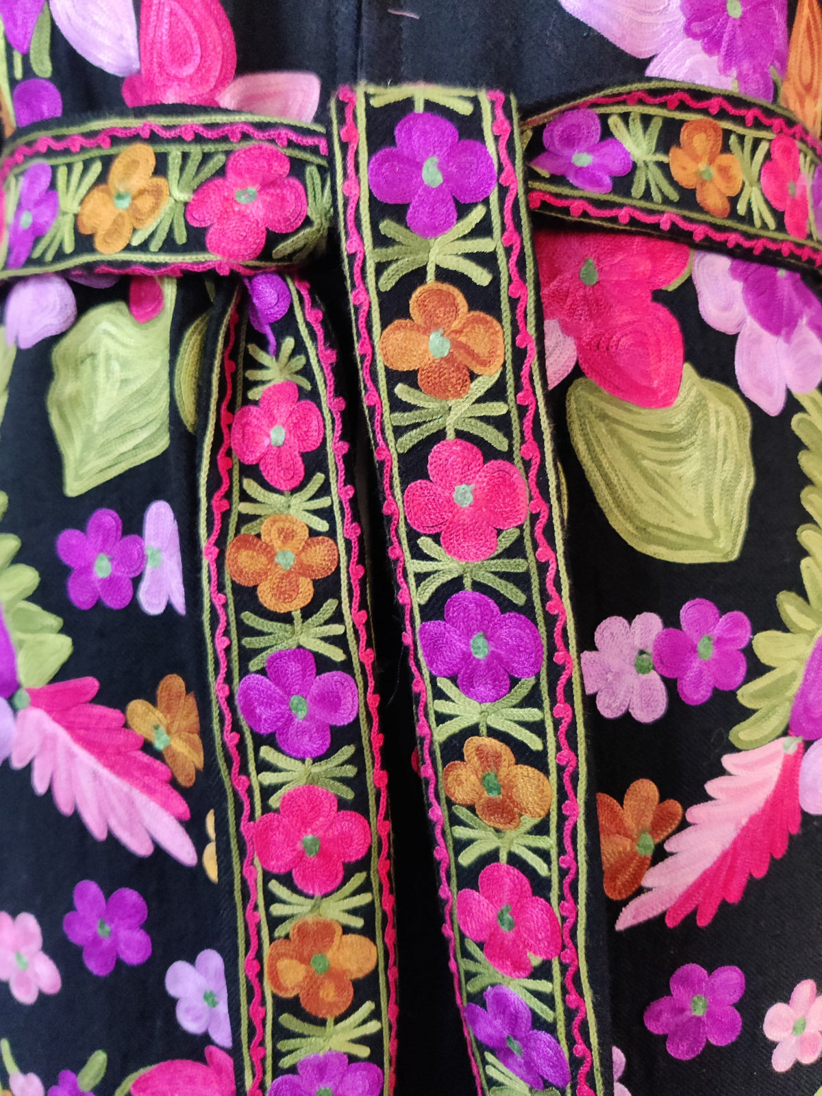 Close-up of the black robe's embroidered belt, with pink, purple and orange flowers, green stems and pink zigzag edging.