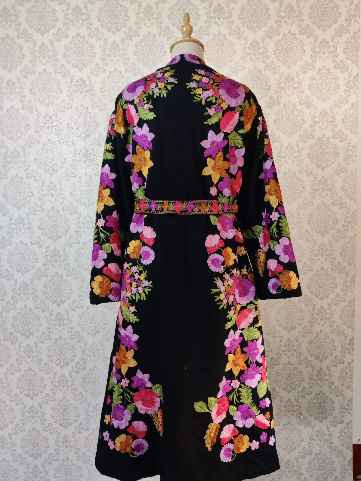 Back of a long black robe with a floral belt, showing colourful flower sprays along the sides around a plain centre.