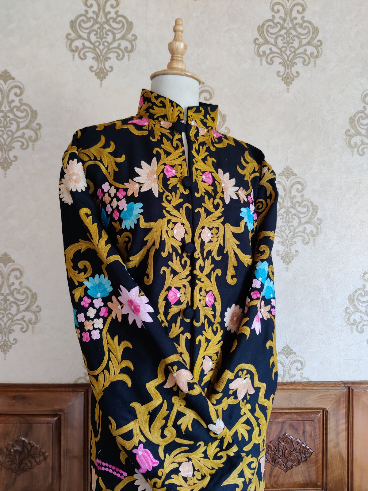 Angled upper front of a black coat showing golden Aari leaves and pink flower buds around the stand collar and front opening