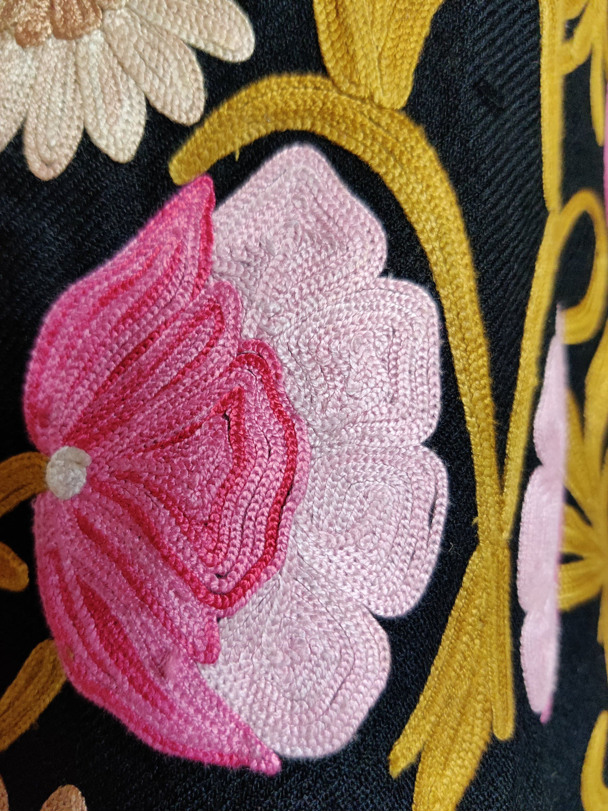Macro view of a pink Aari flower with golden stem and a pale beige blossom on black coat fabric