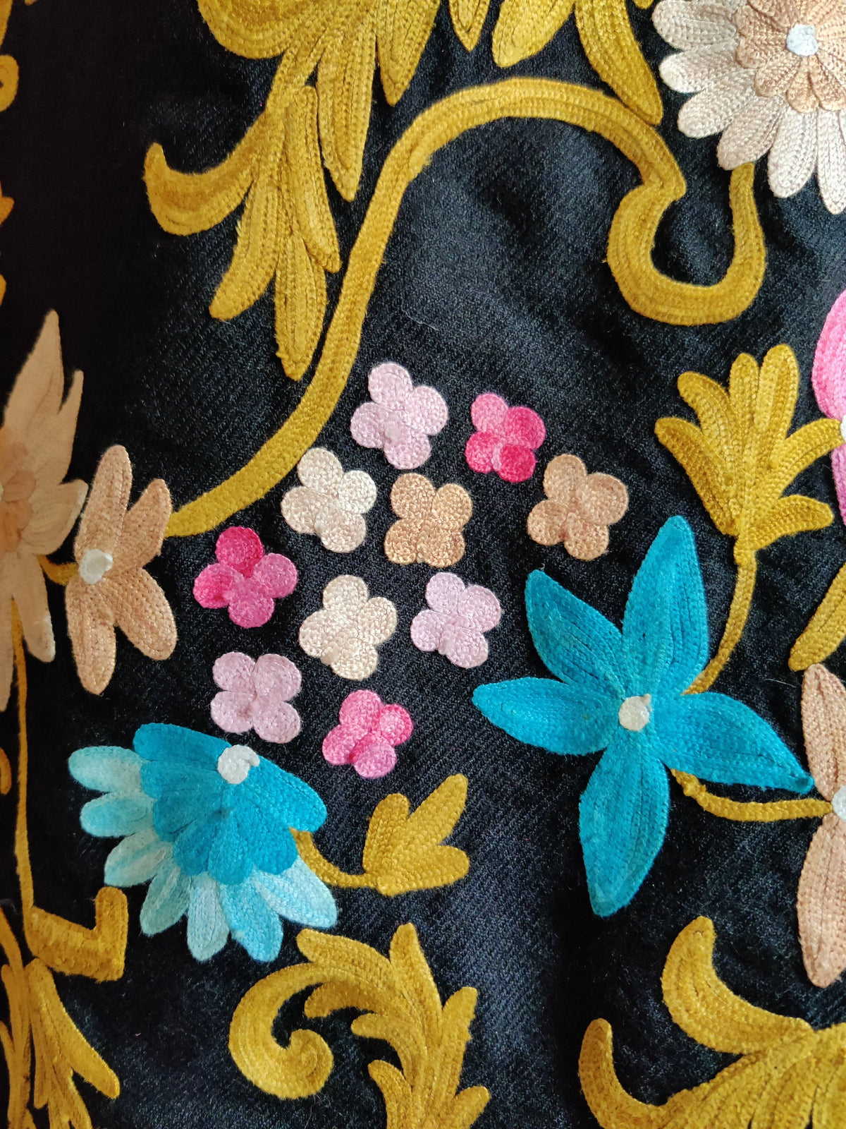 Close-up of blue Aari flowers and tiny pink and beige blossoms among golden scrolling leaves on a black coat
