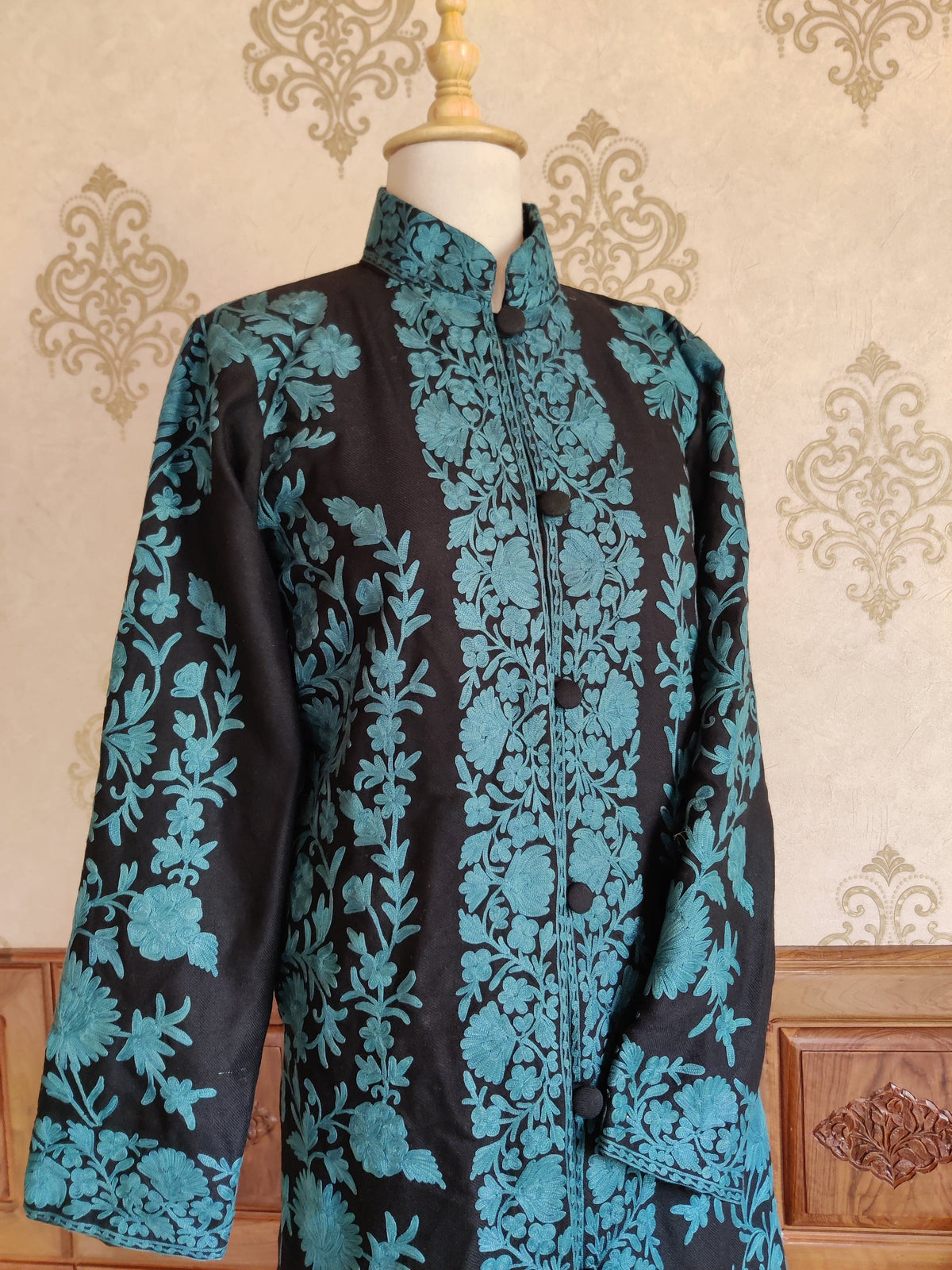 Upper front of the black Aari jacket, showing turquoise floral borders around the collar, buttoned opening and cuffs.
