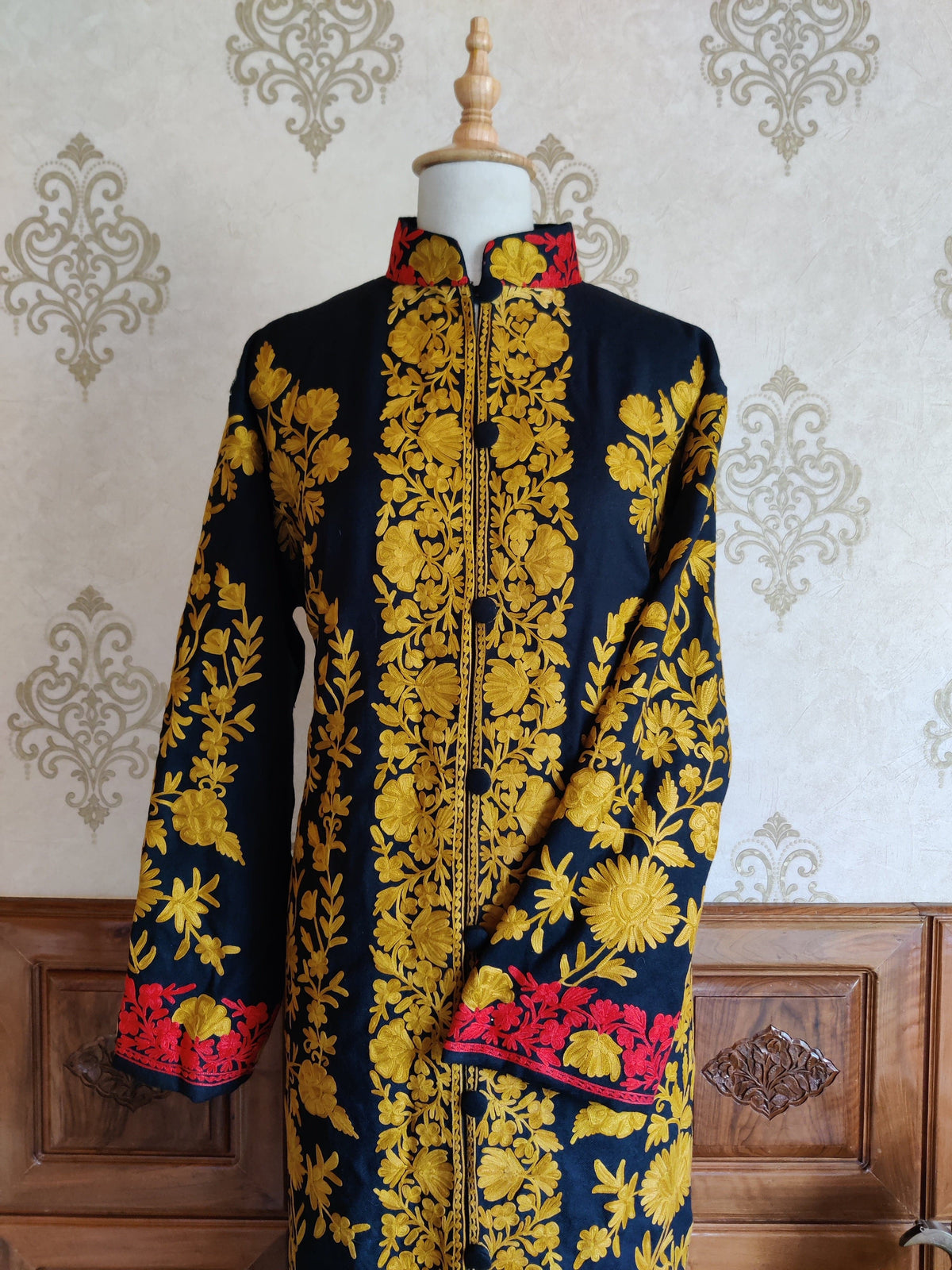 Front view of a navy jacket with mustard-yellow floral embroidery, red cuff borders and a stand collar.