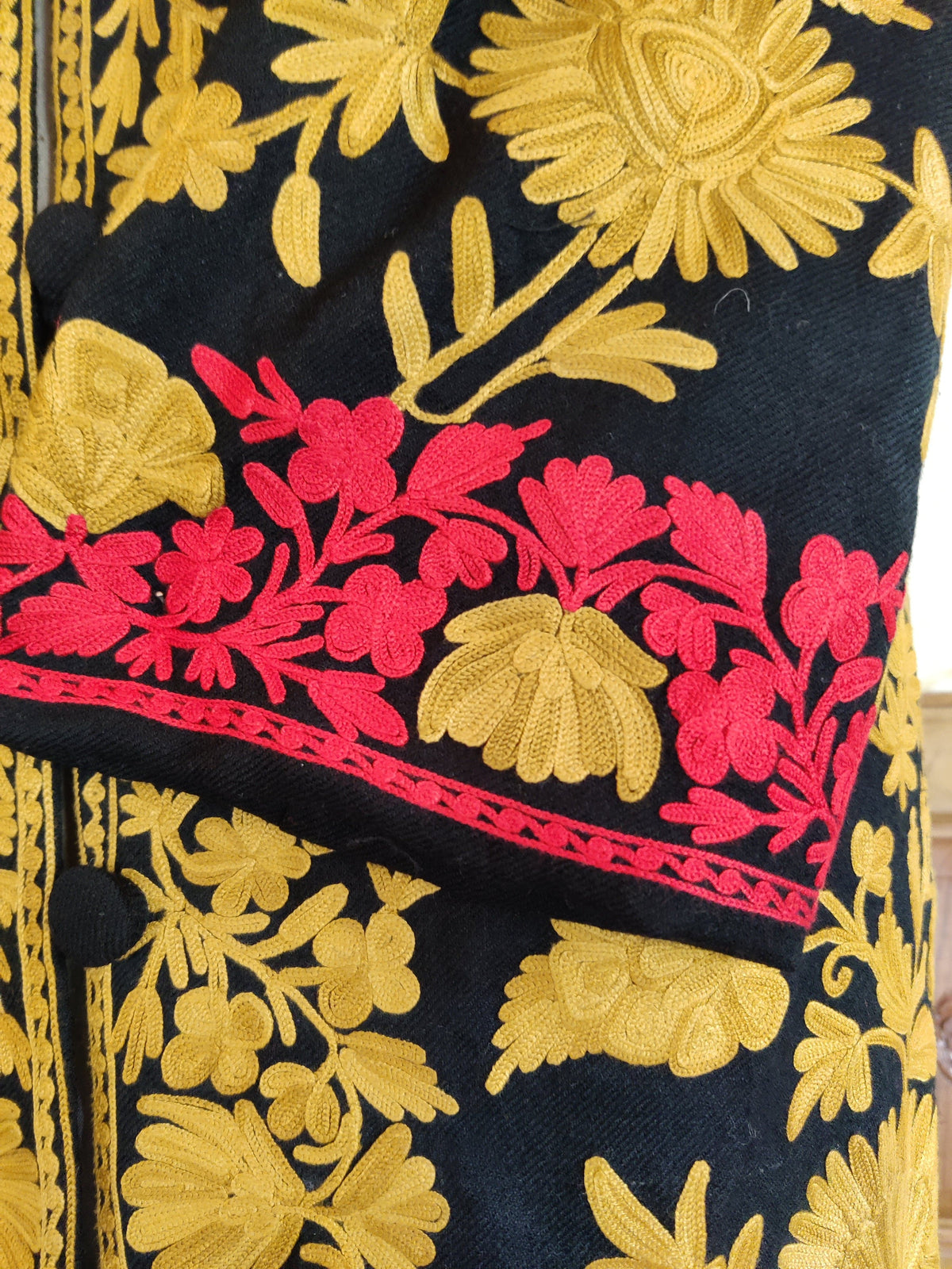 Close-up of the navy jacket’s cuff with red flowers, mustard-yellow blooms and a narrow red stitched edge.