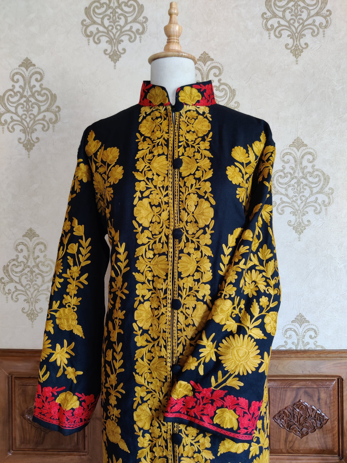 Front detail of a navy jacket with mustard-yellow floral vines, dark buttons and red floral cuff embroidery.