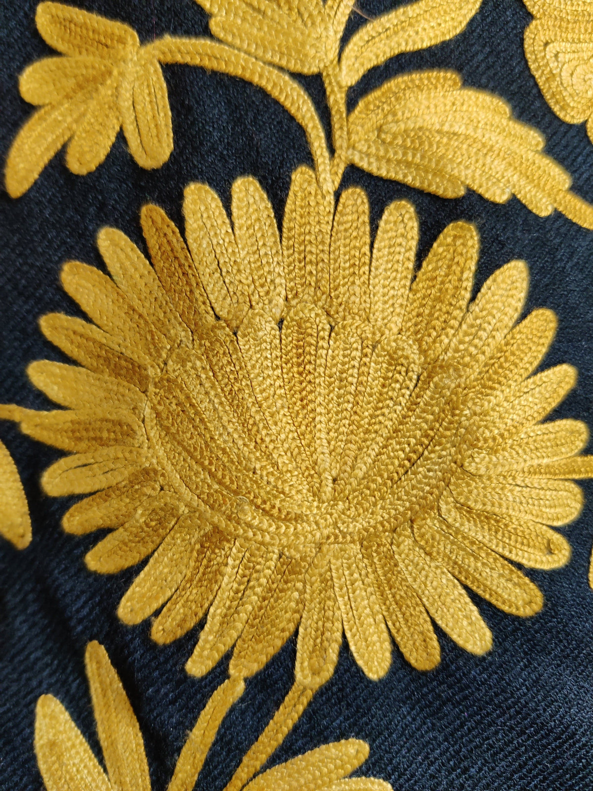 Macro detail of a mustard-yellow embroidered flower and leafy stem on navy fabric.