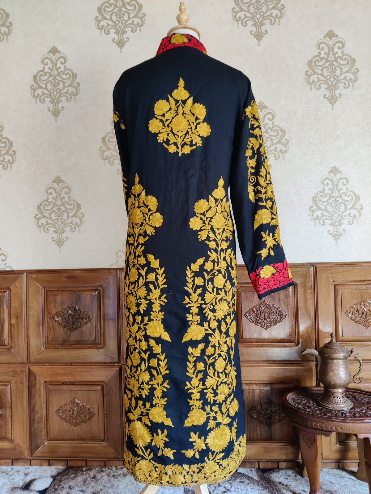 Back of a long navy jacket with mustard-yellow floral sprays, a central upper motif and red cuff borders.