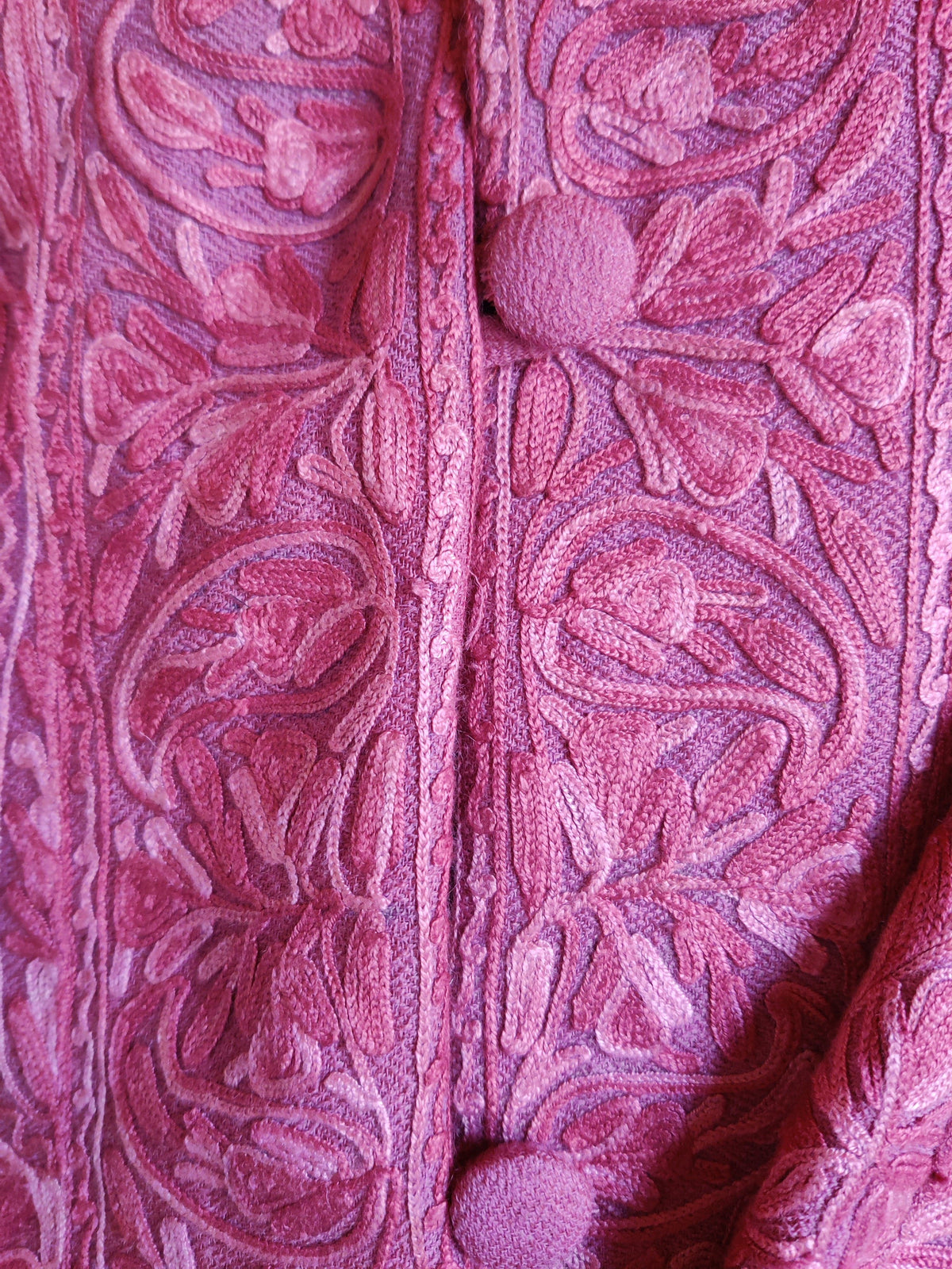 Macro detail of a covered pink button and tonal Aari floral scrolls beside the jacket’s front opening.