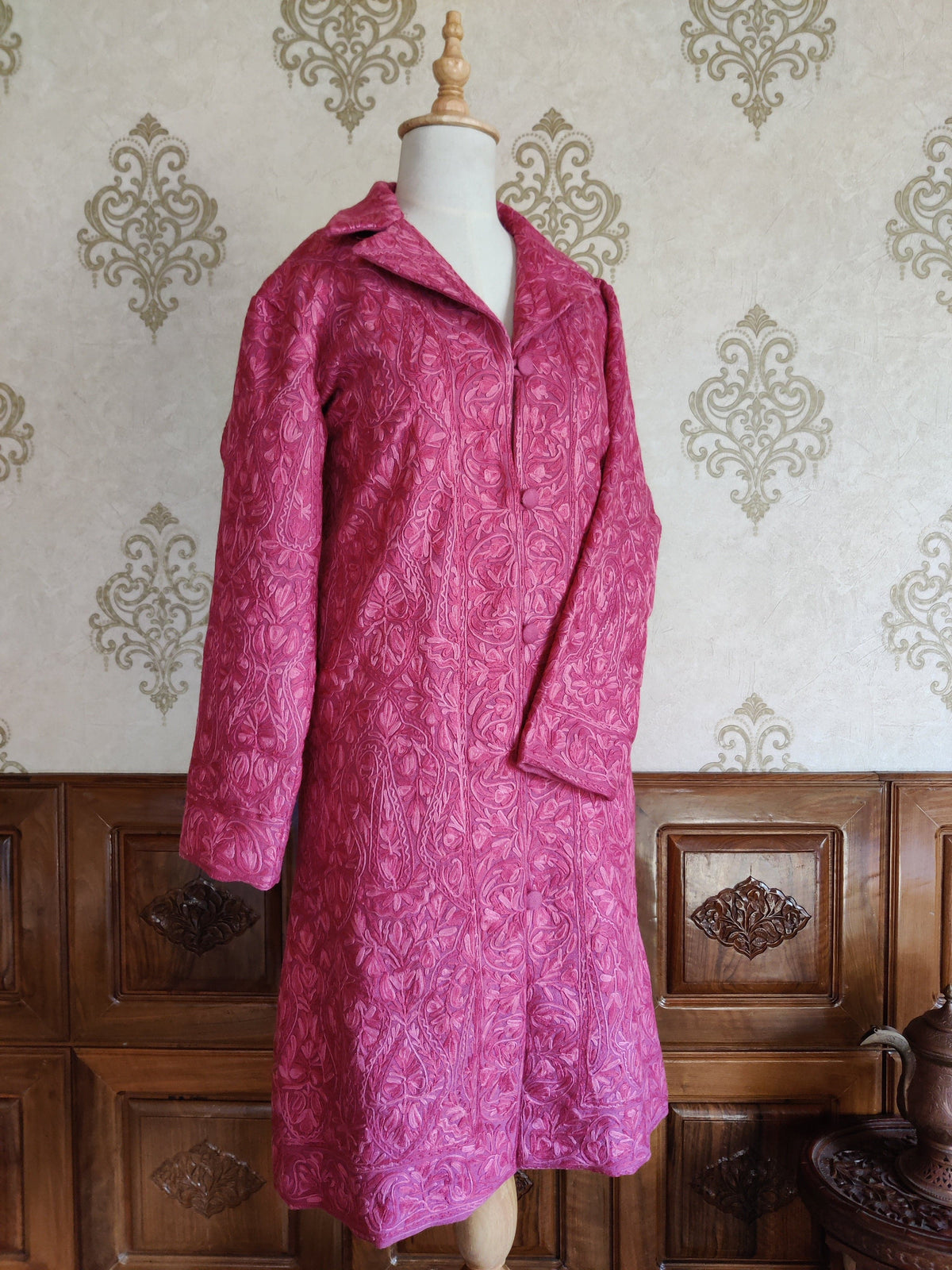 Full front of the long pink Aari jacket on a mannequin, with one sleeve folded over its embroidered body.