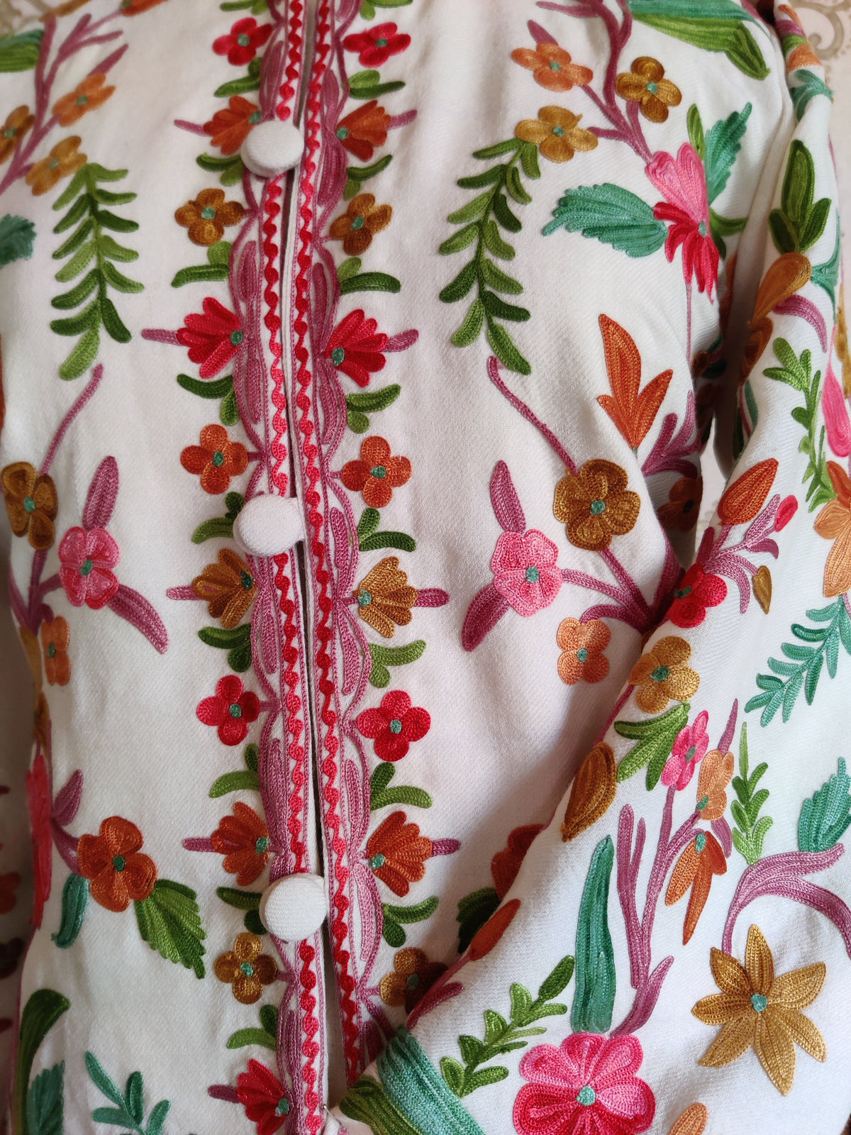 White jacket chest and folded sleeve with pink, red and orange Aari flowers beside the buttoned floral placket