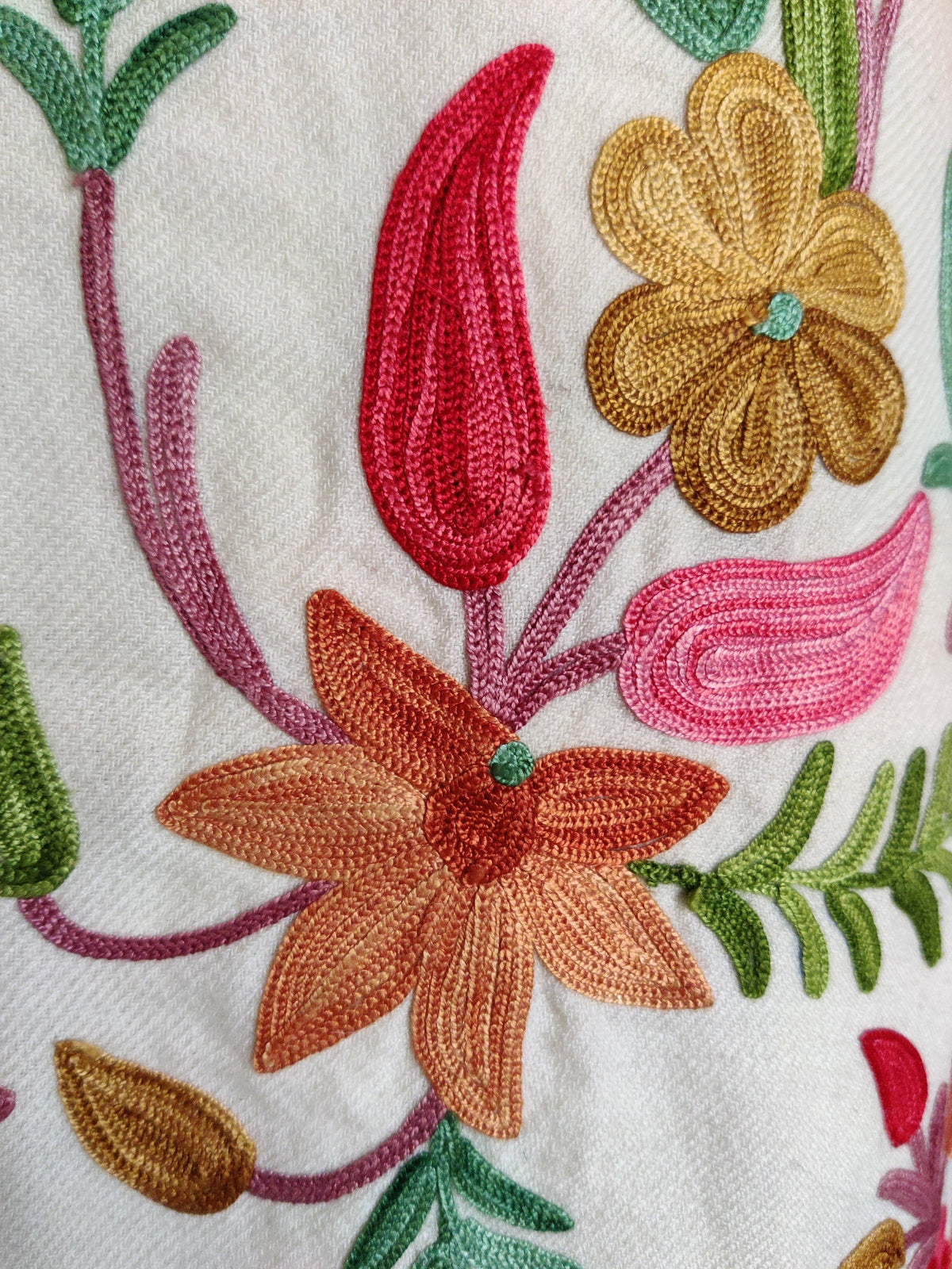 Close-up of peach and ochre Aari flowers, red and pink leaves and curling mauve stems on a white jacket