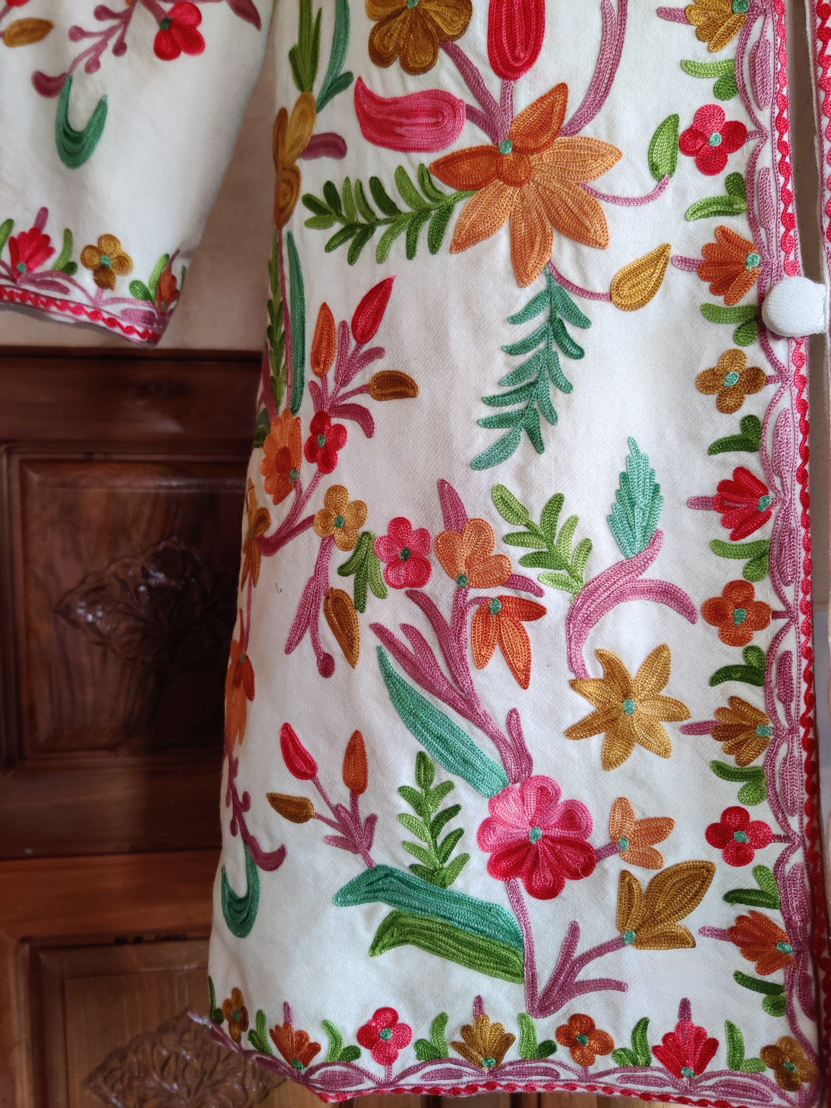White jacket lower front with orange and pink Aari flowers, green leaf sprays and pink edging beside the buttons