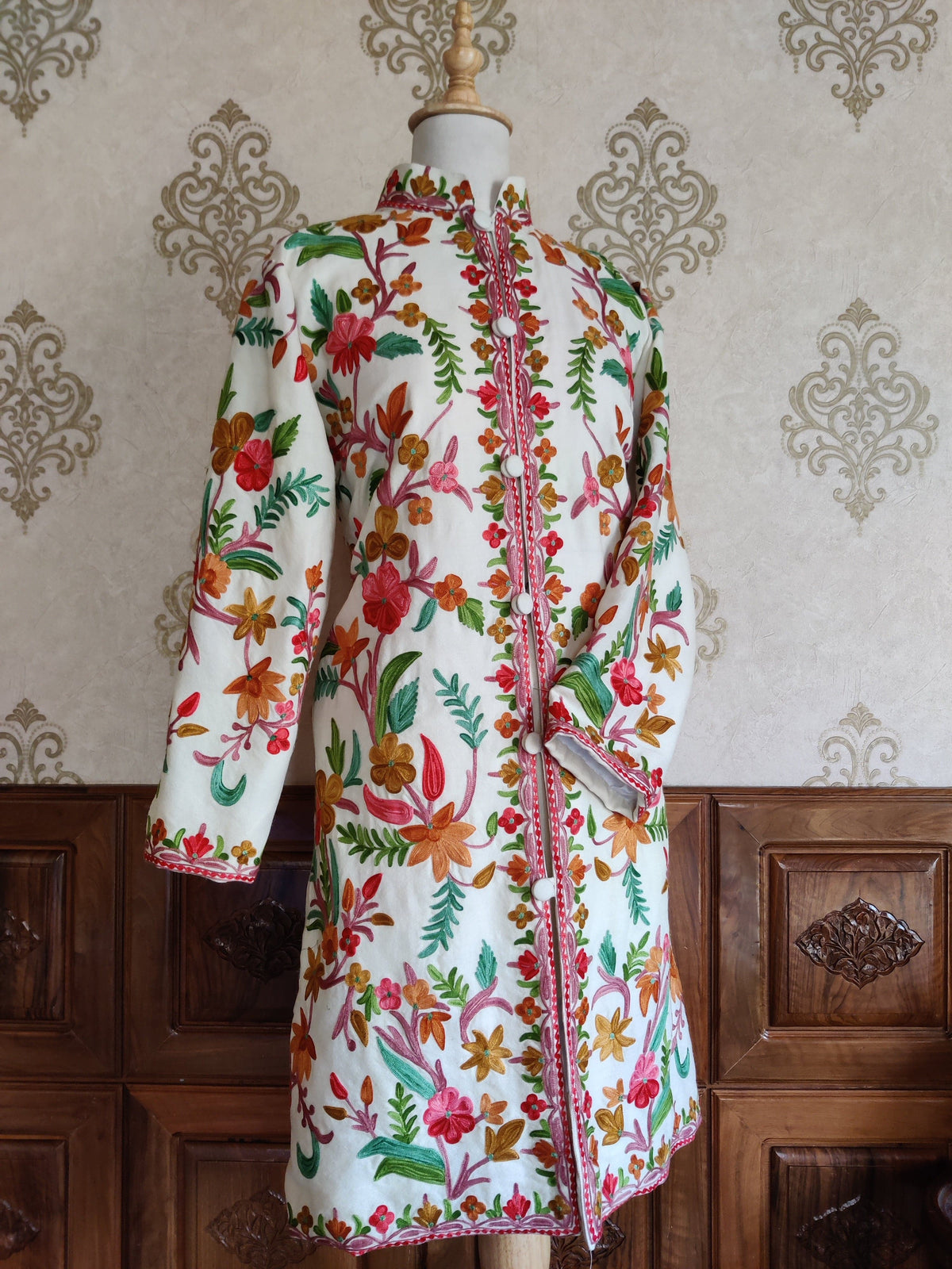 Full-length angled front view of a white Aari jacket with colourful floral vines and one sleeve bent across the waist