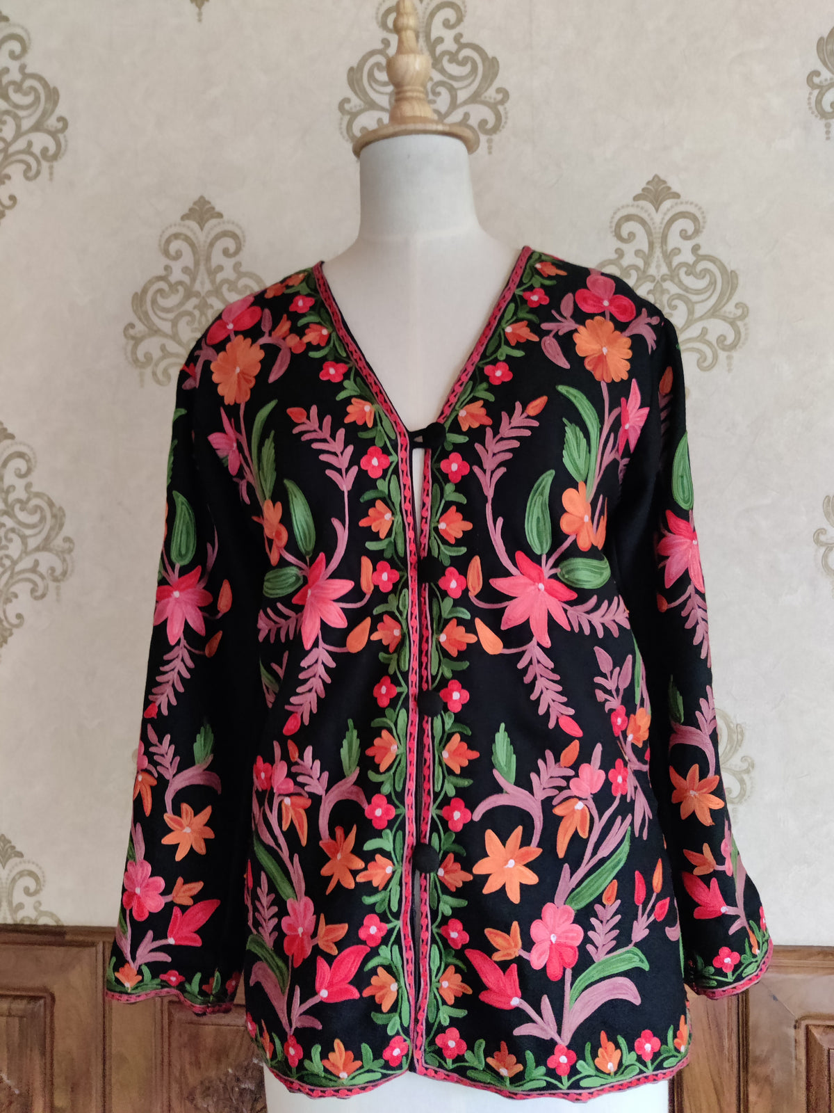 Full front of a black short jacket with pink and orange Aari floral vines and a narrow embroidered V-neck border