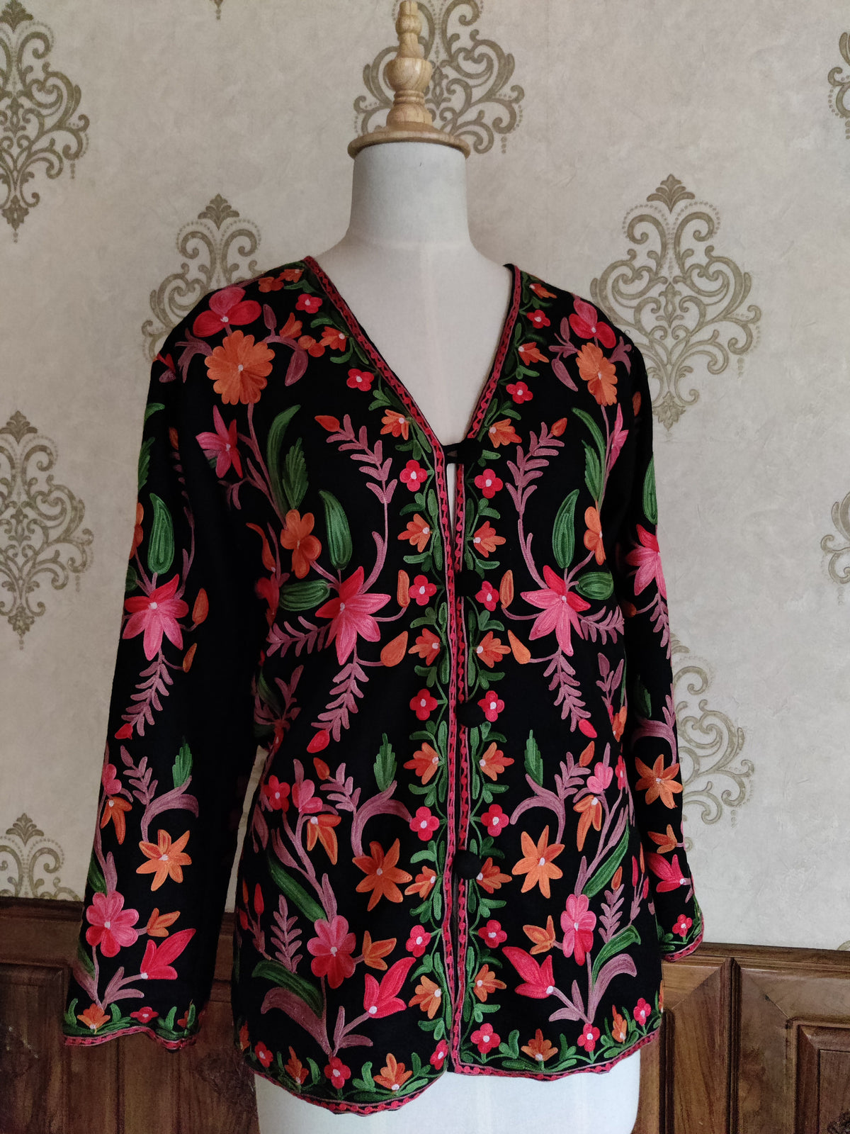 Angled front of a black short jacket with bright Aari flower sprays, pink stems and green leaves