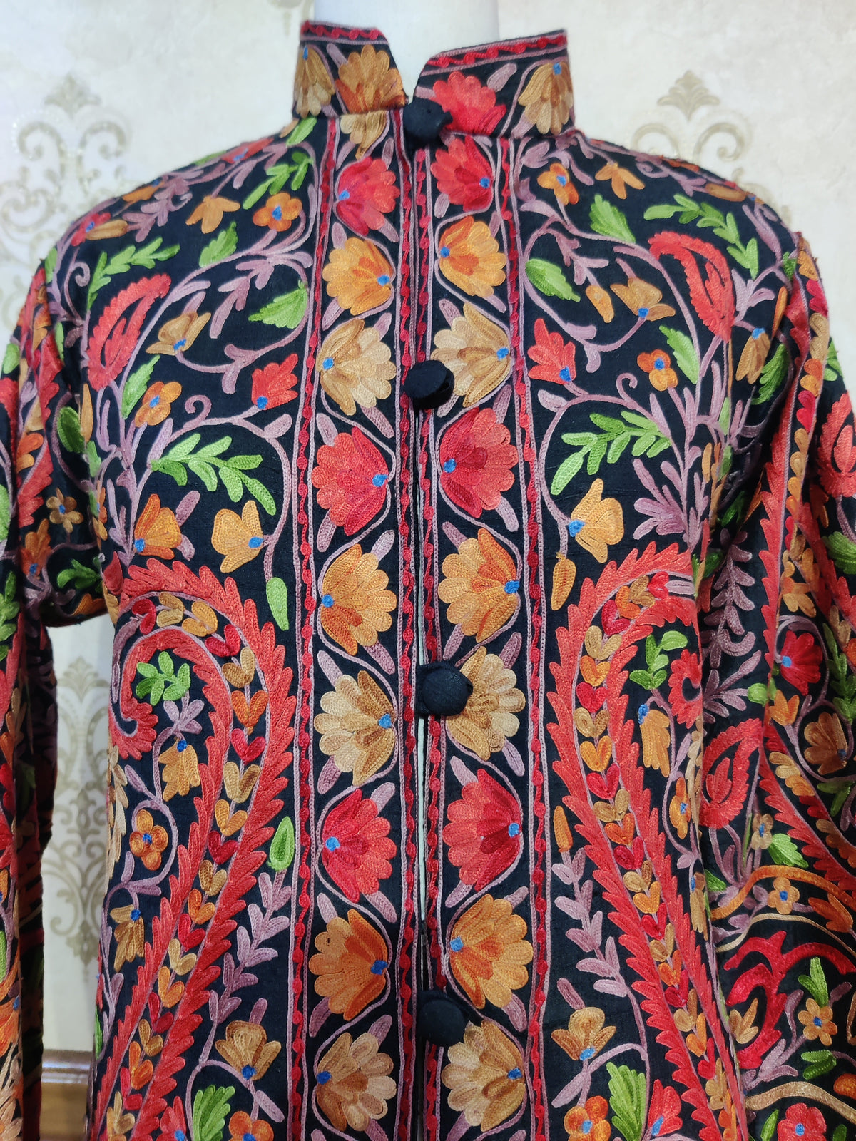 Close-up of the standing collar and black buttons on the jacket, surrounded by red, orange and gold Aari flowers.