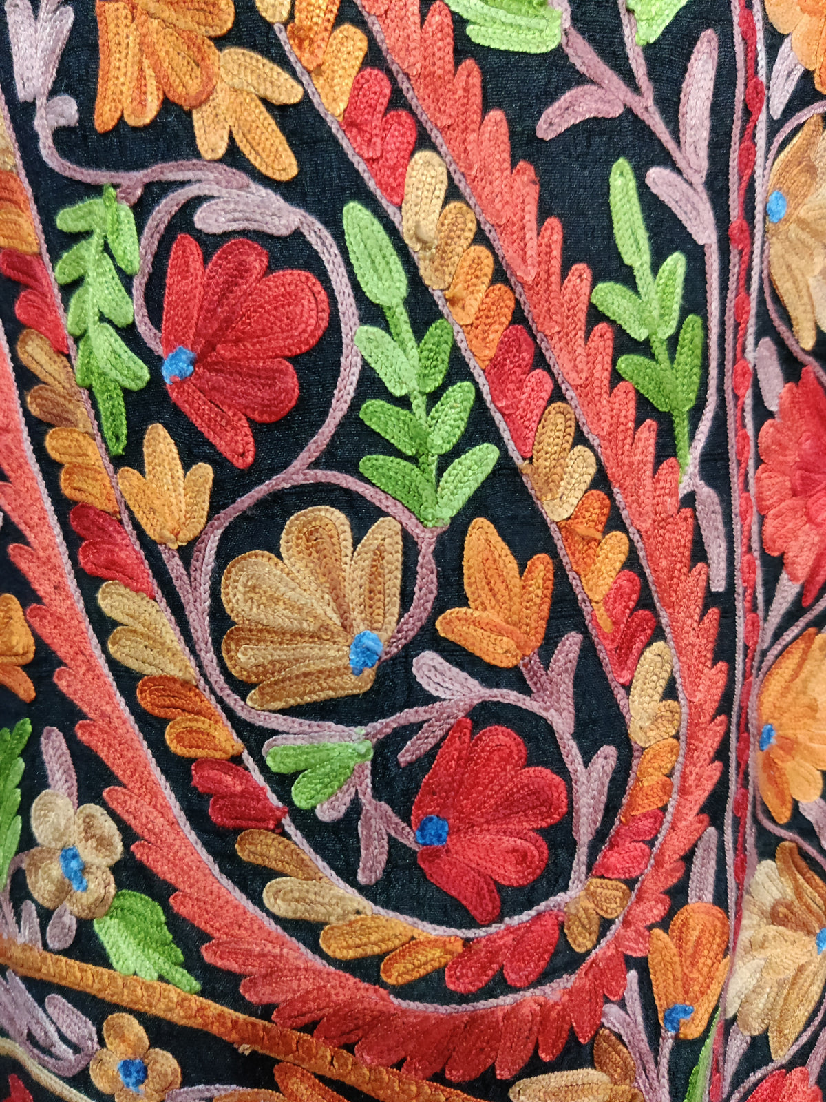 Macro view of red and gold Aari flowers, green leaves and pink stems inside a red-edged paisley on the black jacket.