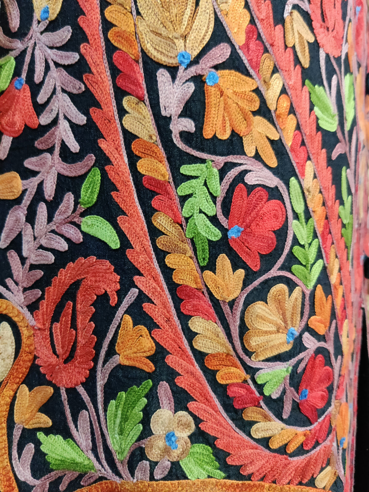 Angled embroidery detail showing red and orange flowers, green leaves and layered Aari stitching on the black jacket.