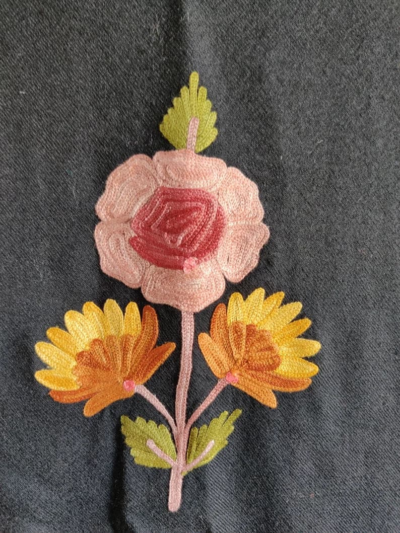 Close-up of a small embroidered bouquet with a pink rose, two yellow flowers and green leaves on black robe fabric