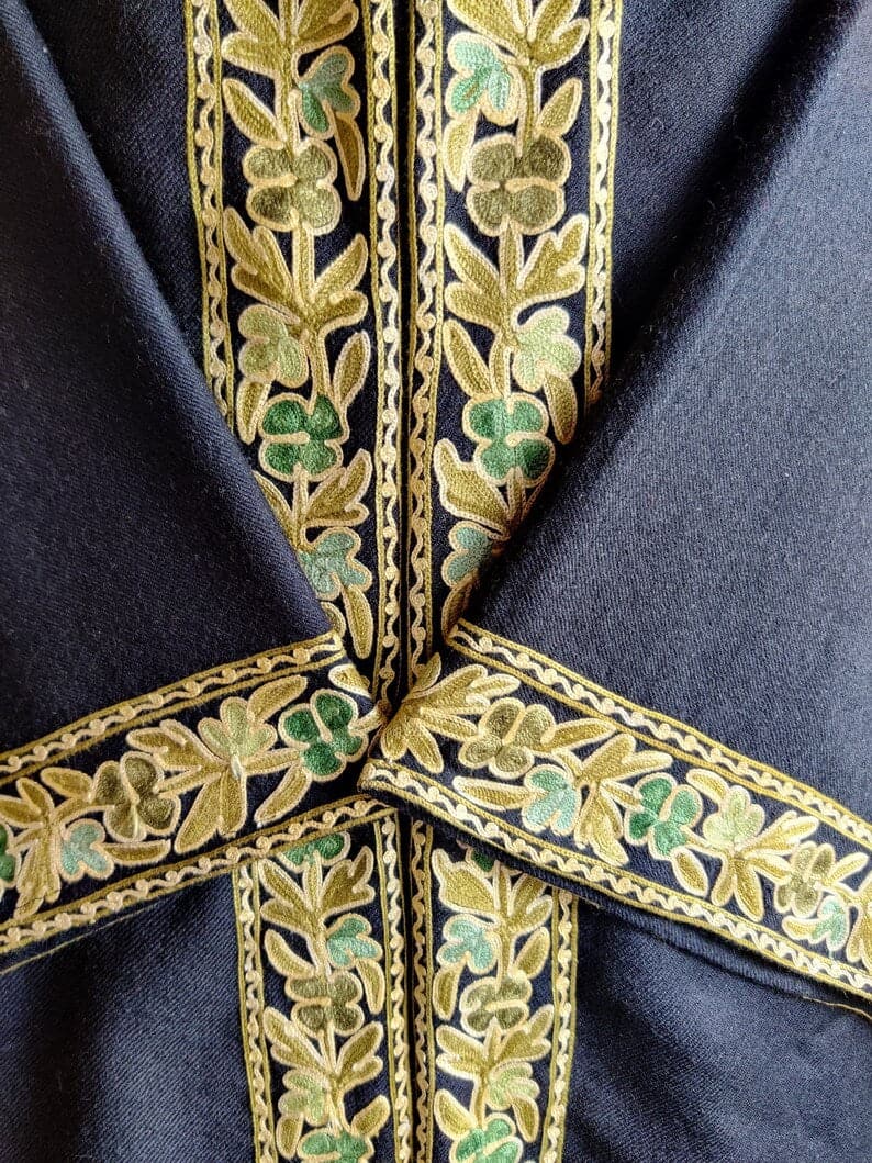 Close-up of crossed black robe cuffs and front borders with gold leaves and green four-petal flowers