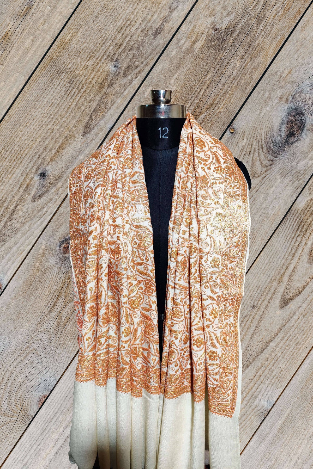 White Merino wool shawl draped around a mannequin's neck, with golden-peach Tilla floral embroidery above plain hanging ends