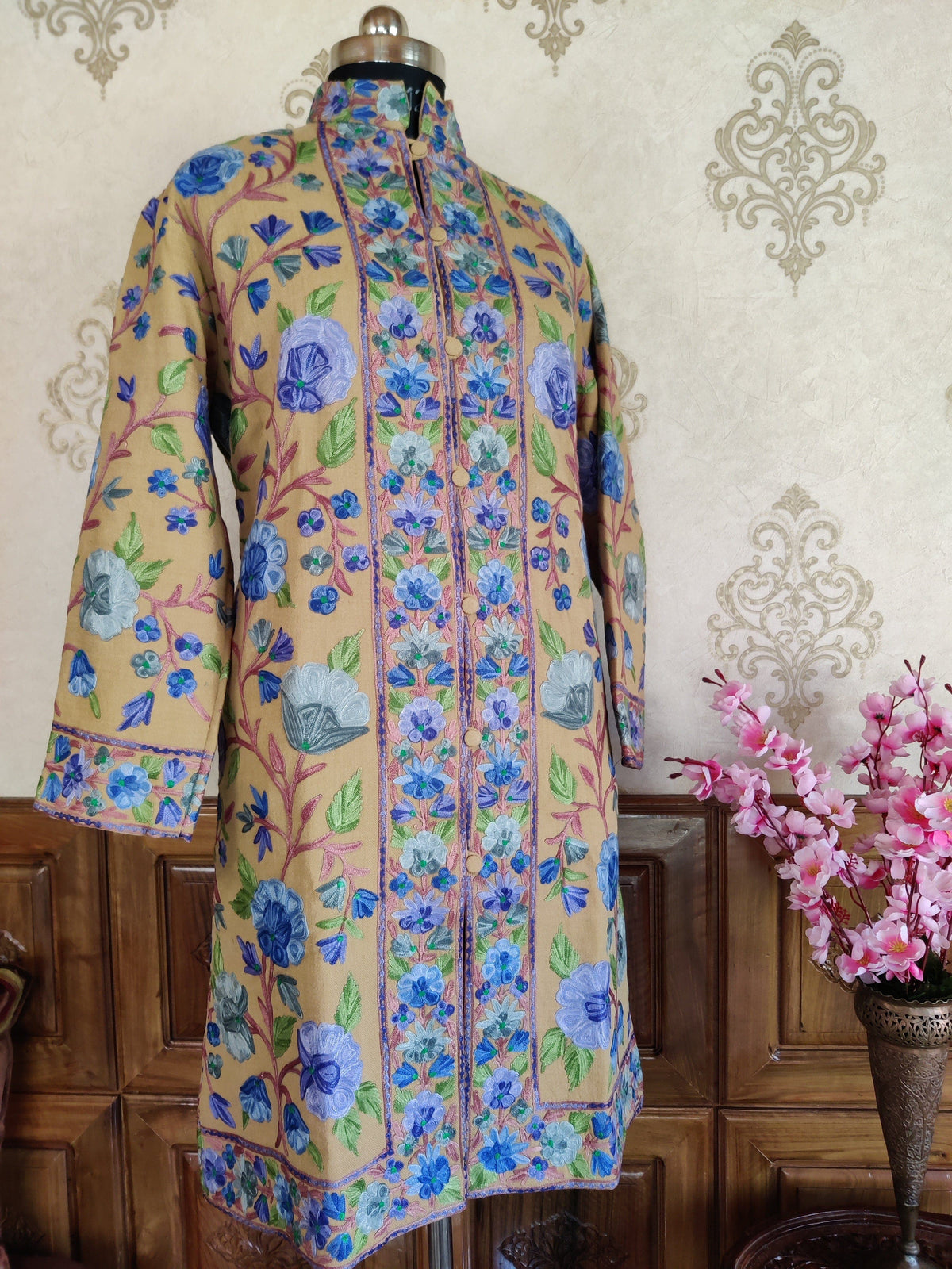 Full front view of a golden-beige jacket with blue floral vines and patterned borders along the front, cuffs and hem.