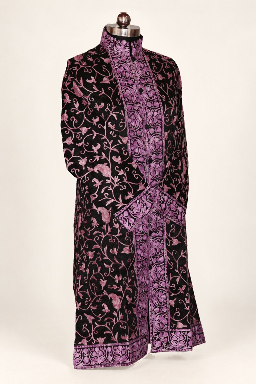 Angled front of a black long coat on a mannequin, with pink-purple Aari vines, a dense floral placket and hem border, and crossed sleeves.