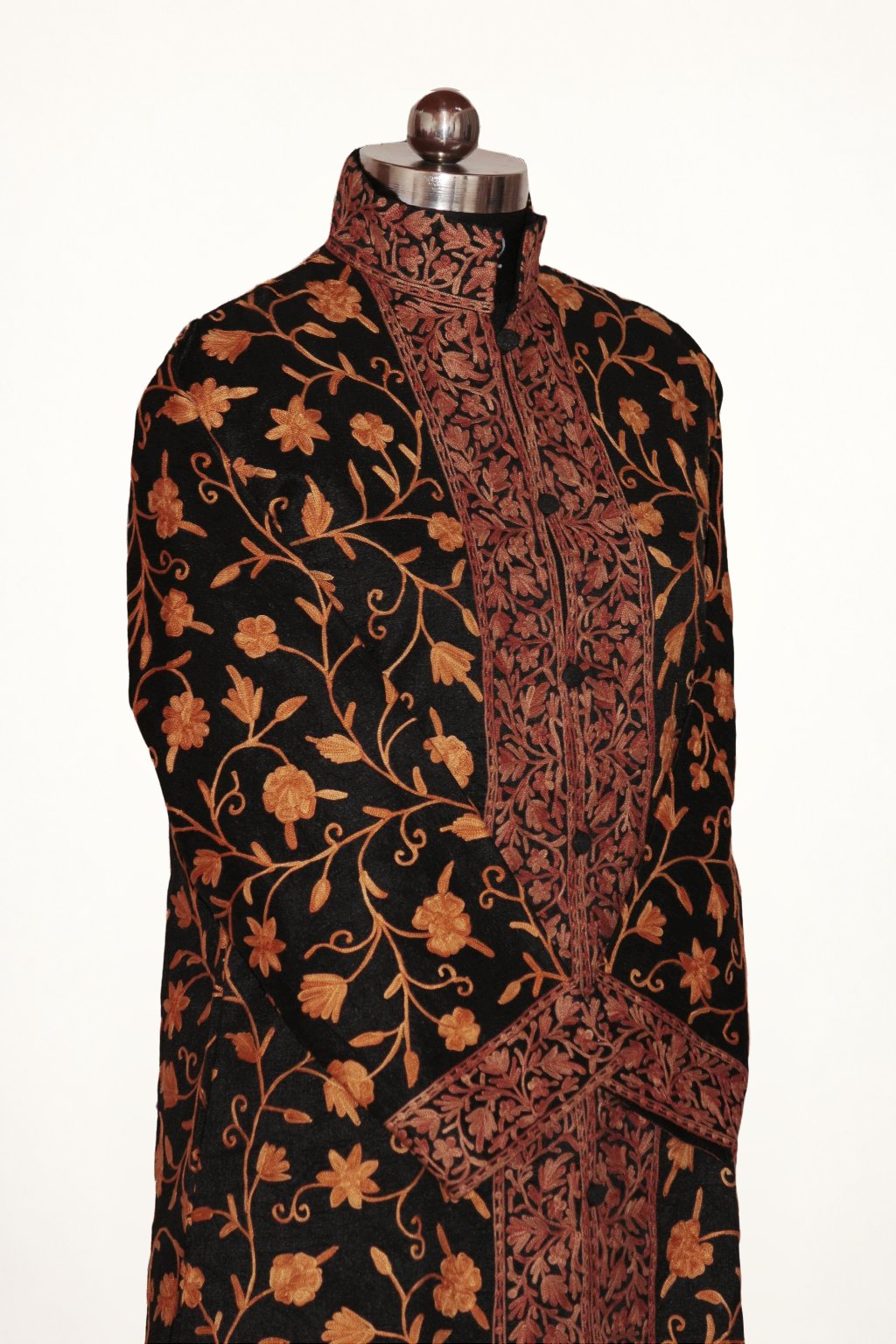 Angled front view of the black long coat, with orange Aari floral vines, broad brown embroidered borders and crossed sleeves