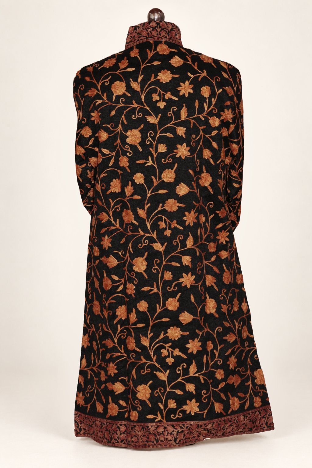 Back view of the black long coat on a mannequin, with orange Aari floral vines and brown embroidered collar and hem borders