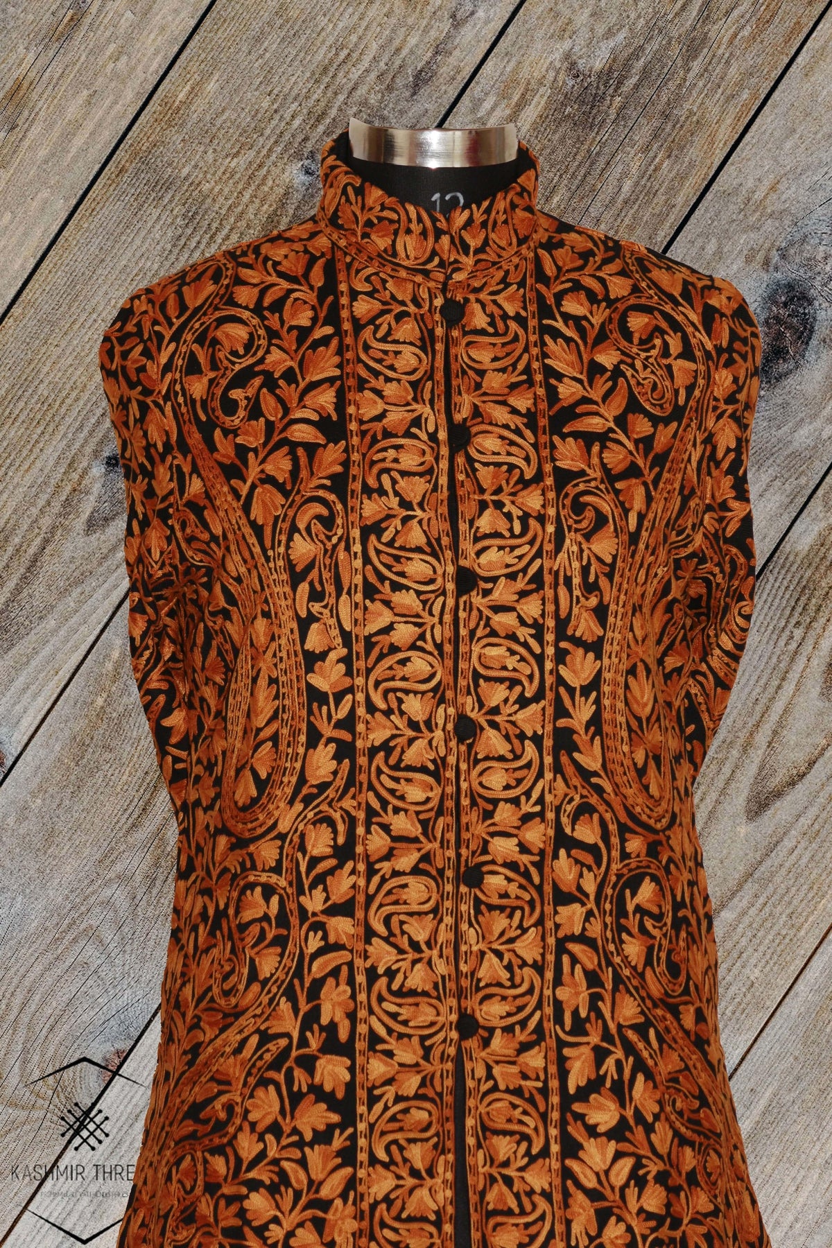 Front view of the black jacket on a mannequin, with dense orange-brown Aari paisley embroidery and a stand collar