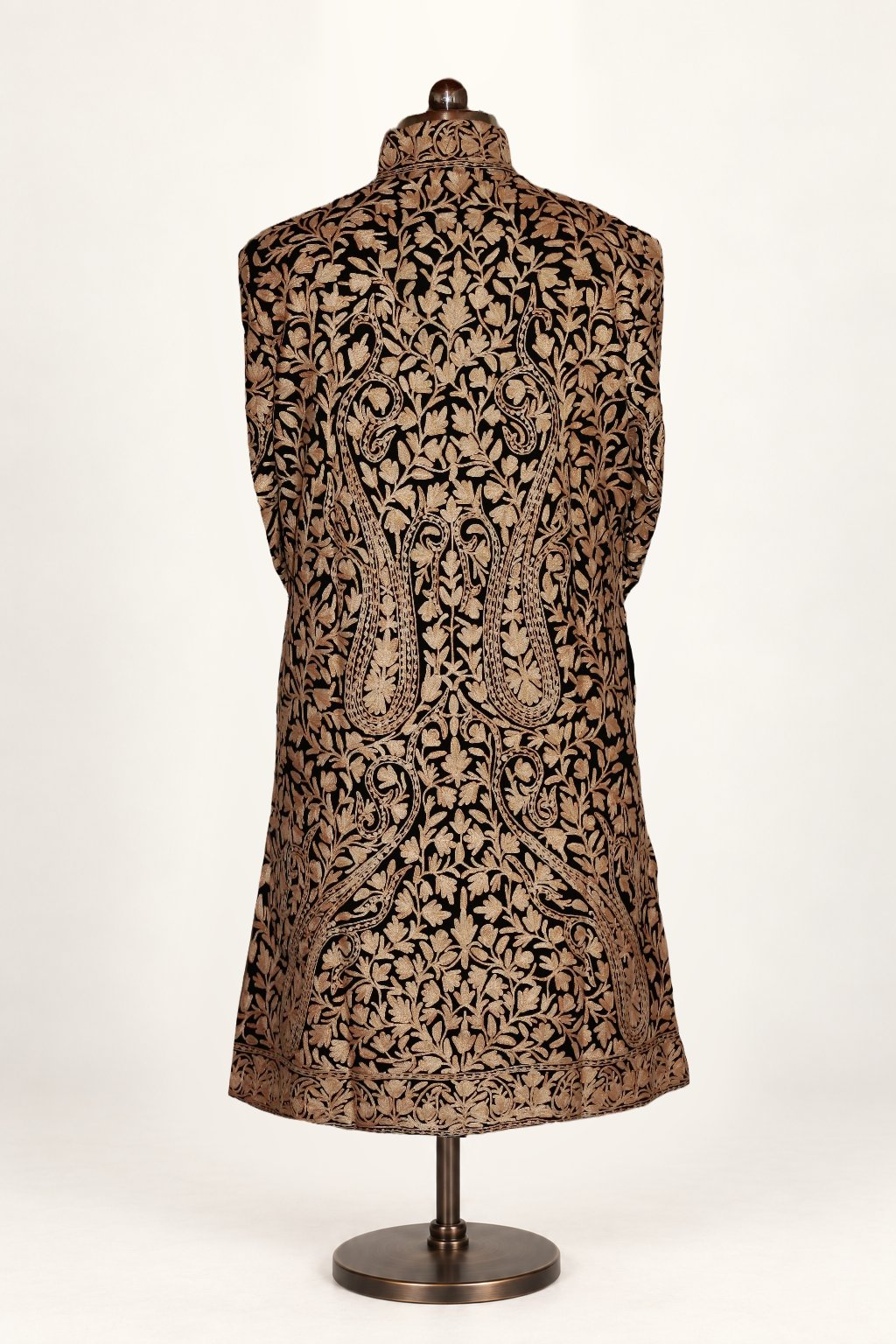 Back of a black wool jacket on a mannequin, with large gold-toned Aari paisleys among dense floral vines and a matching hem border.