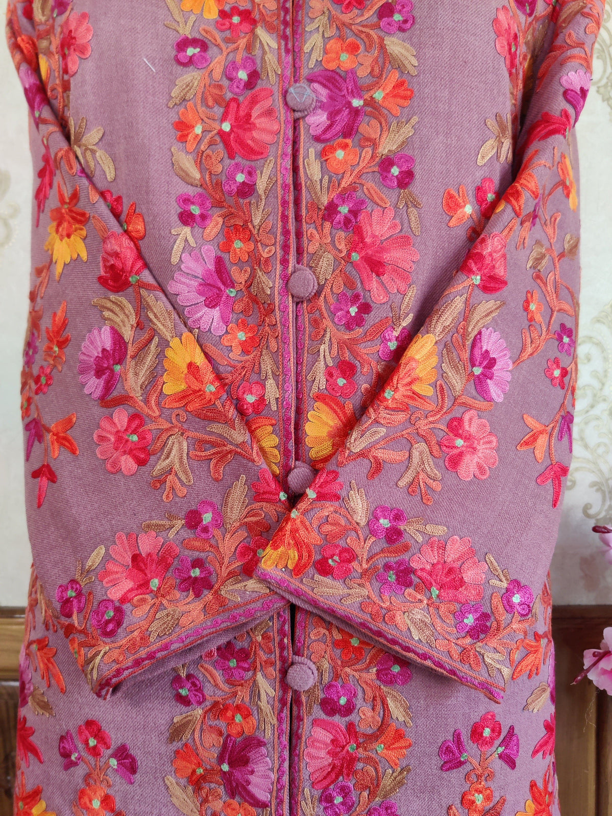 Close-up of crossed cuffs and covered buttons on a mauve coat with pink, orange and yellow Aari floral embroidery
