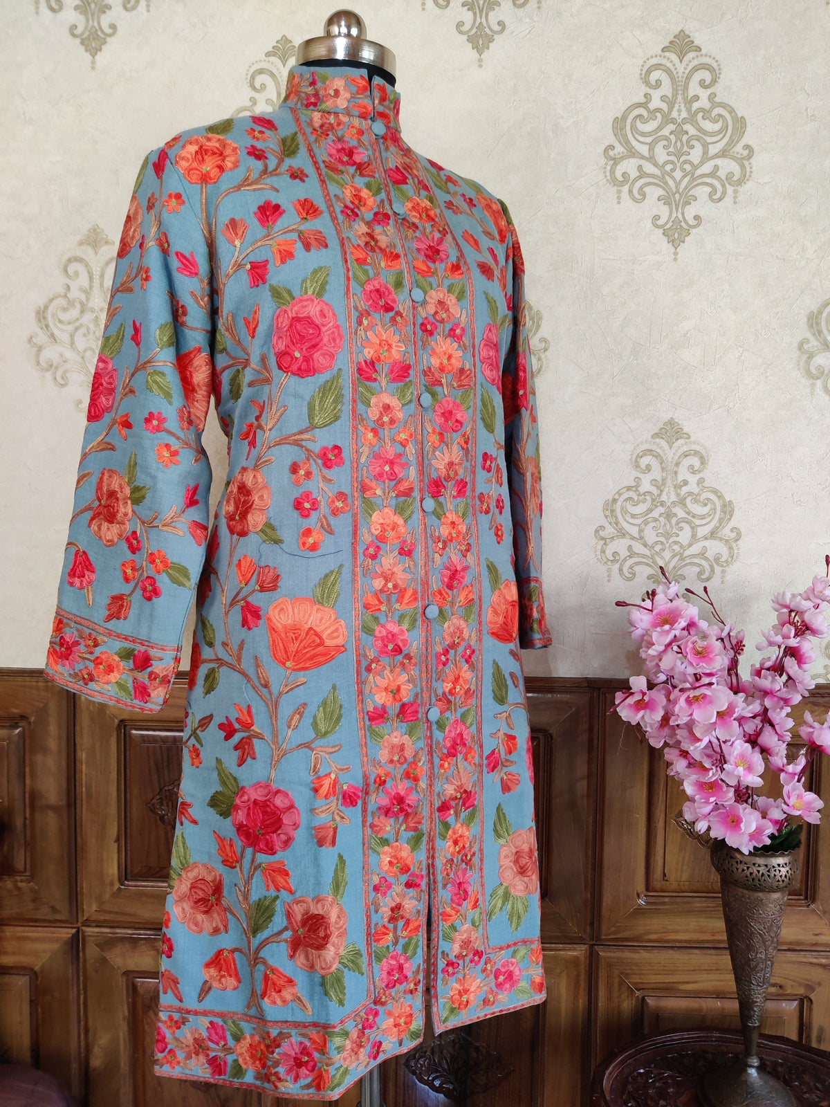 Full front view of an azure-blue jacket with coral floral vines, a band collar and embroidered borders at the front, cuffs and hem.
