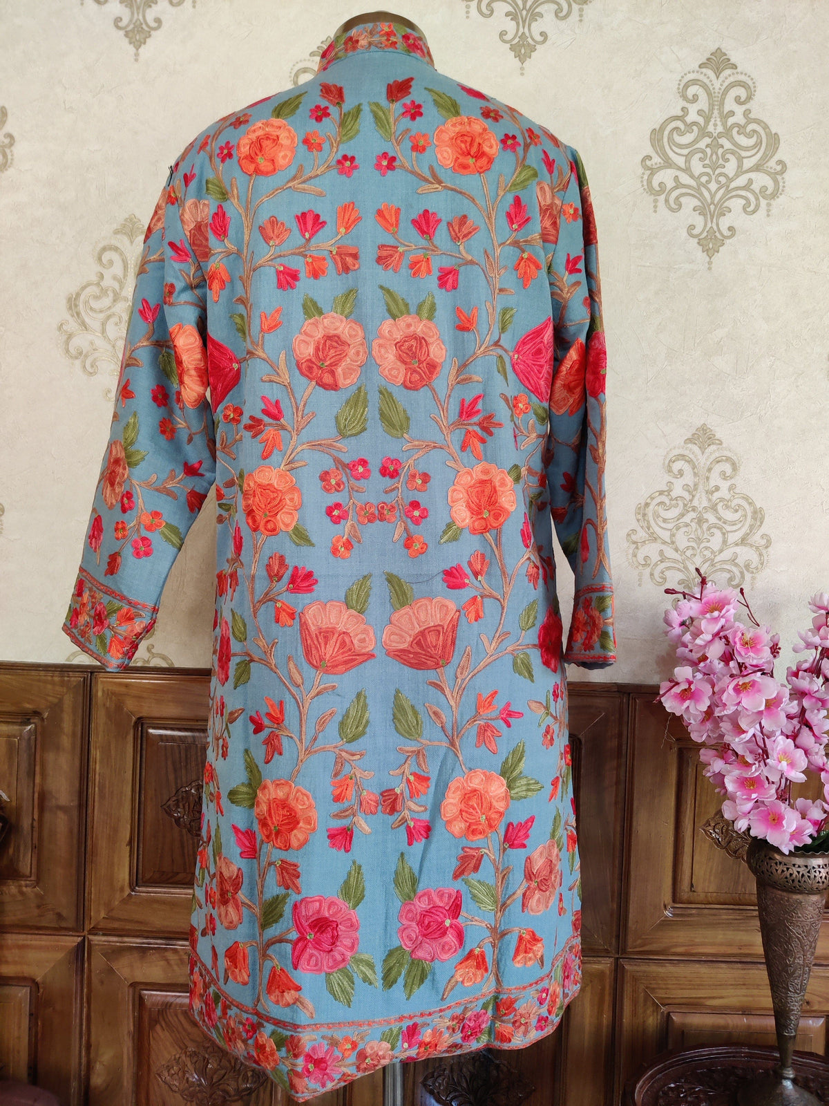 Back of an azure-blue jacket with symmetrical coral and rose floral vines and green leaves.