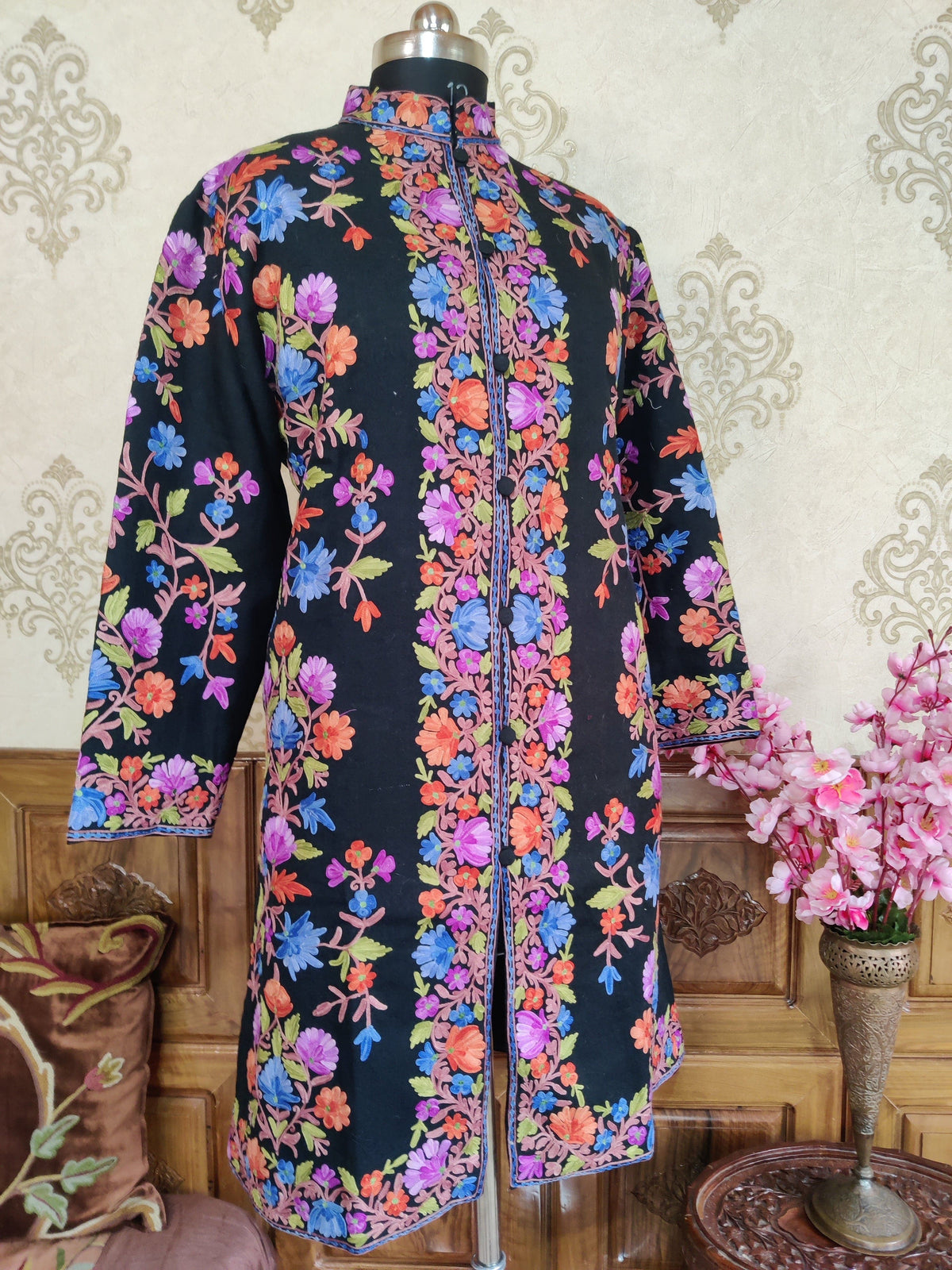 Full front of a black long coat with sleeves hanging, showing colourful Aari floral vines and dense flowered front borders