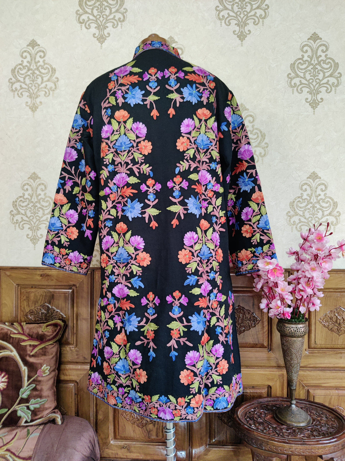 Back of a black long coat with symmetrical blue, purple and orange Aari floral vines and a narrow flowered hem