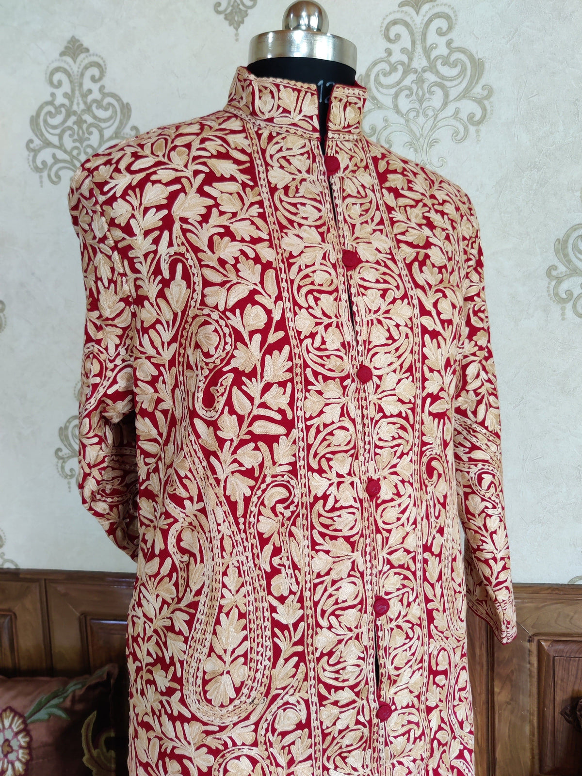 Upper front detail of the maroon jacket showing cream leafy vines, paisleys and embroidered borders beside the fastening.