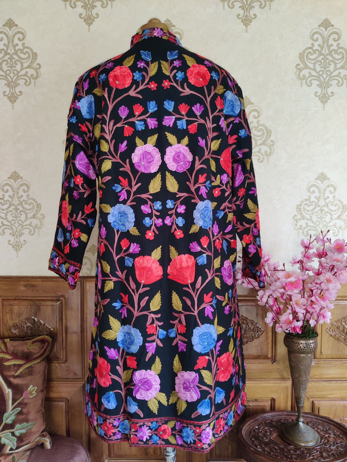 Back view of a black jacket with symmetrical floral vines in blue, purple and red, and a narrow floral hem border.