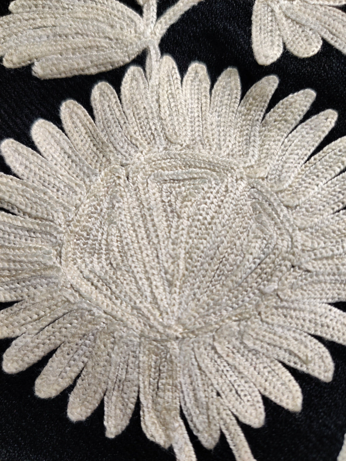 Macro view of the stitched centre and long petals of a pale daisy-like flower on the black jacket
