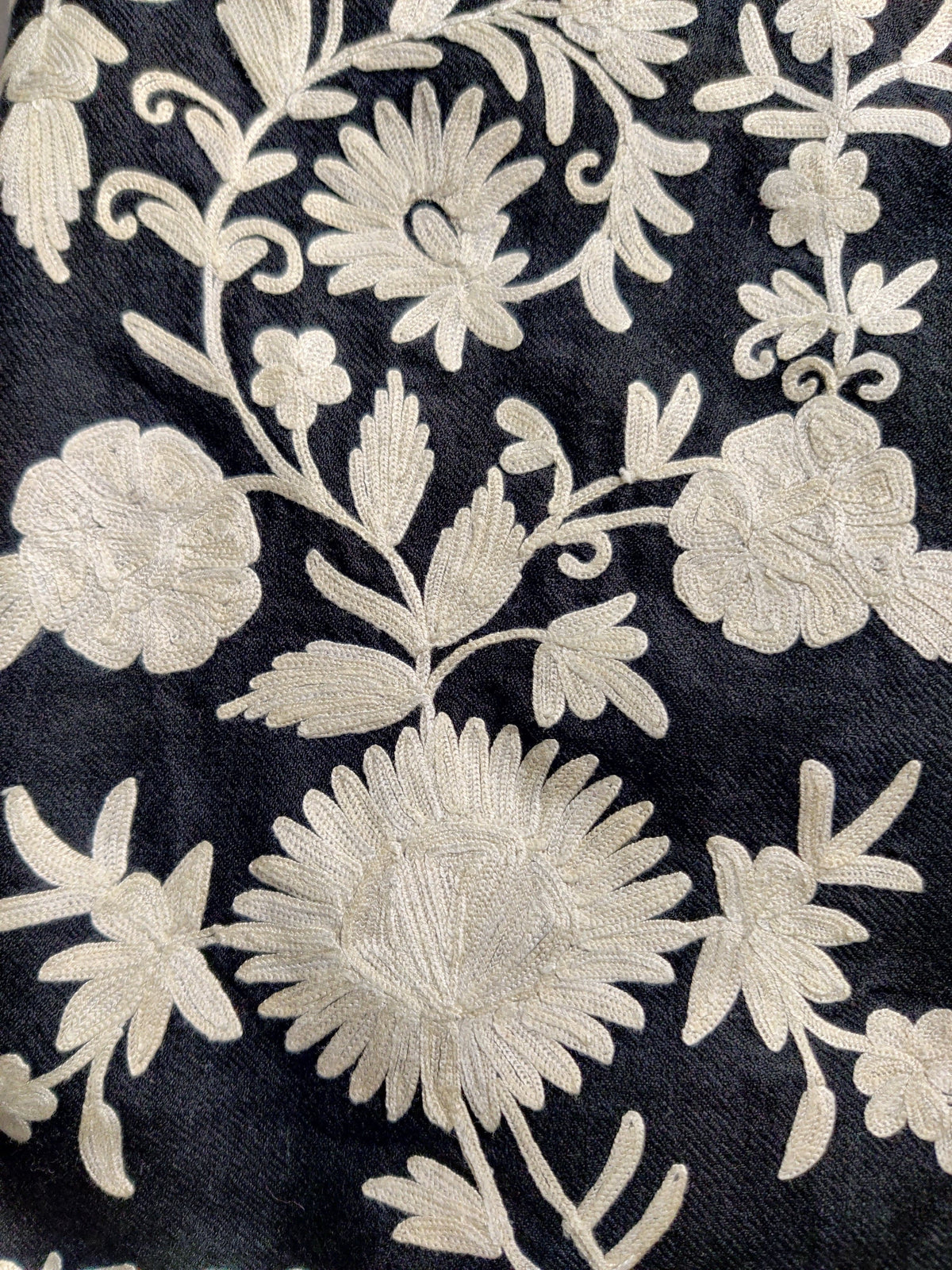 Close-up of white Aari flowers, buds and curling leafy stems embroidered on the black jacket