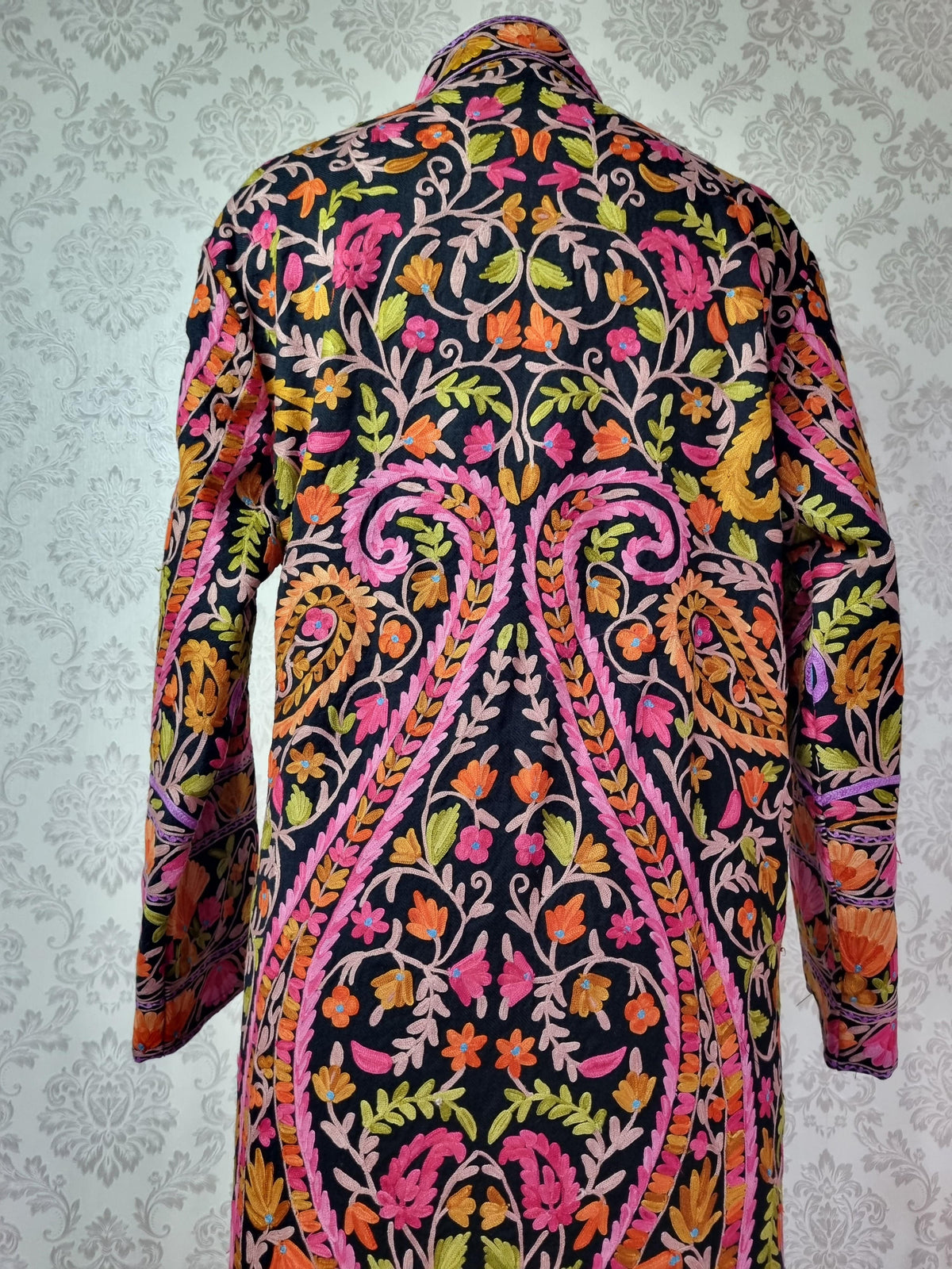 Upper back of the black jacket showing symmetrical pink-edged paisleys filled with colourful flowers and leafy vines.