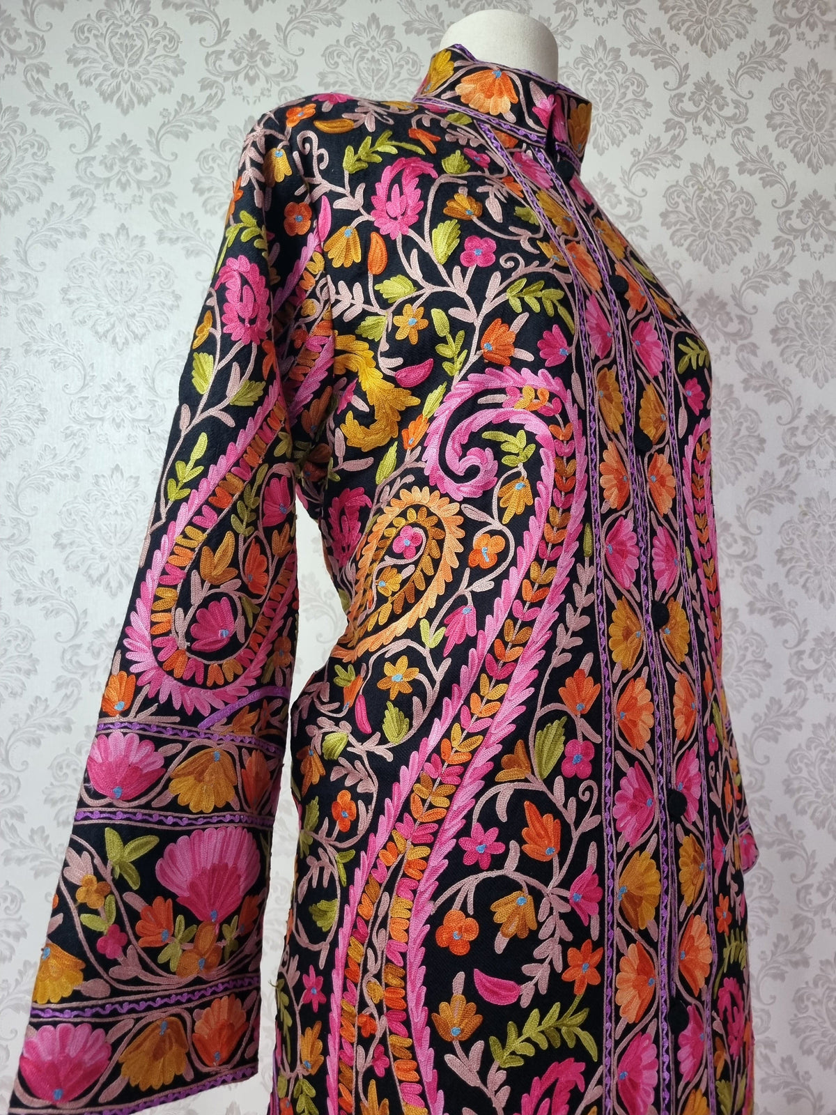 Angled shoulder and sleeve view of the black jacket with bright floral vines, large paisleys and a stand collar.
