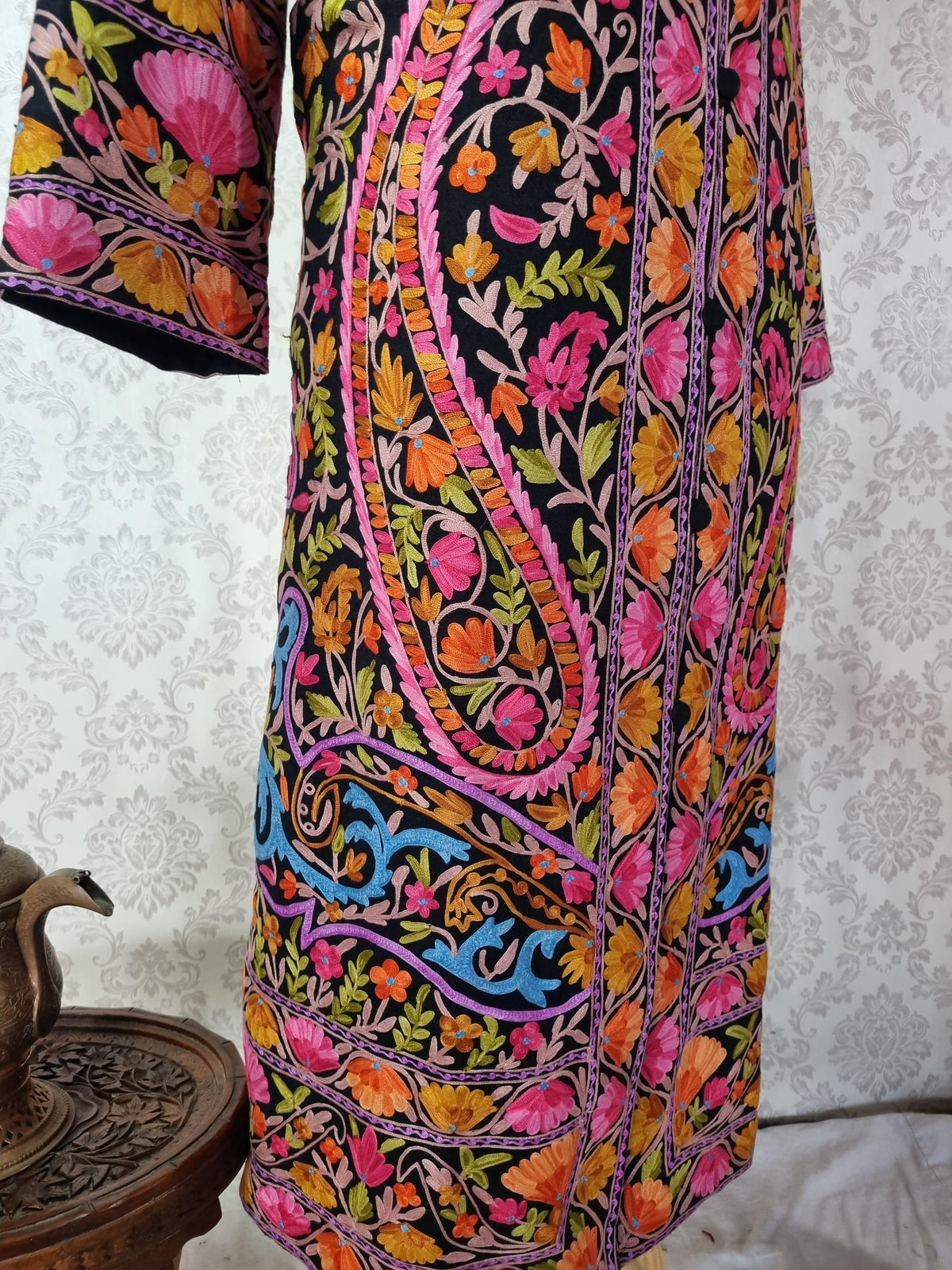 Lower front detail of the black jacket with large pink-edged paisleys, colourful floral vines and layered hem borders.