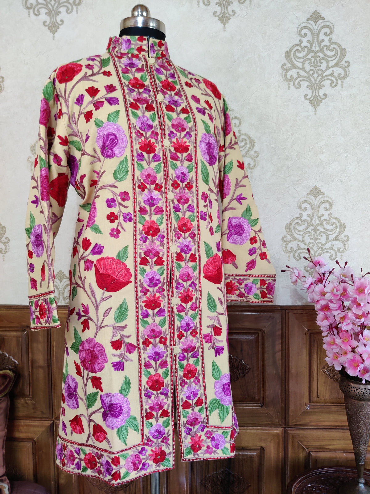 Full front of a cream long jacket with sleeves hanging, showing bright Aari floral vines and dense pink and purple front borders