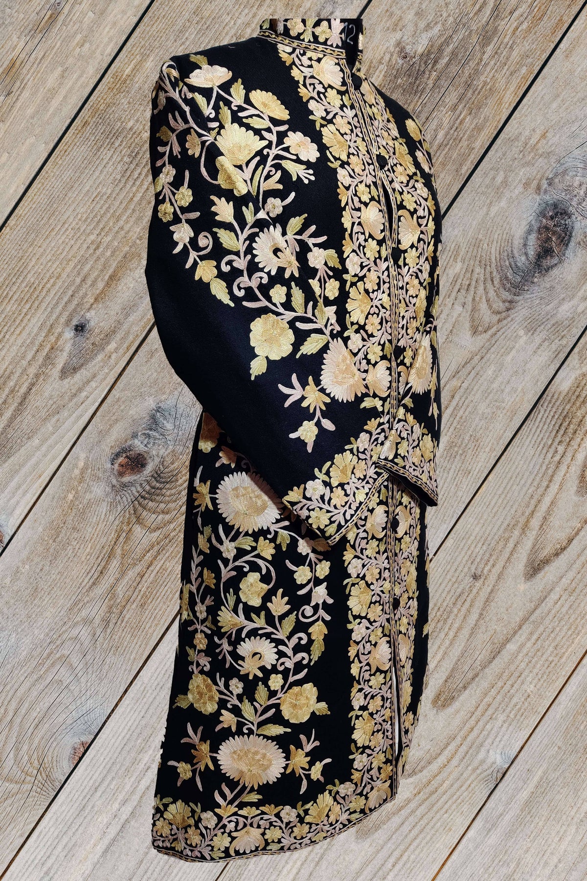 Angled view of a black long jacket with sleeves crossed, showing cream and pale yellow Aari floral vines and matching cuff borders.