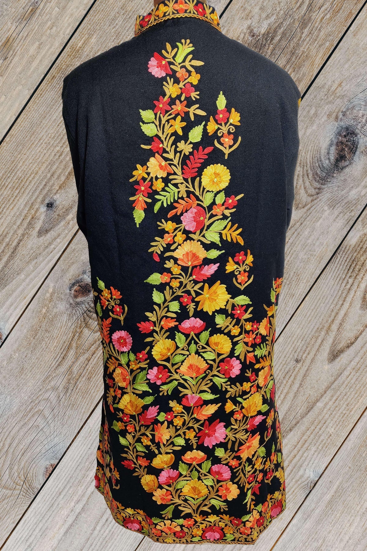 Back of a black long jacket with a central Aari floral vine that widens into a dense multicoloured arrangement near the hem