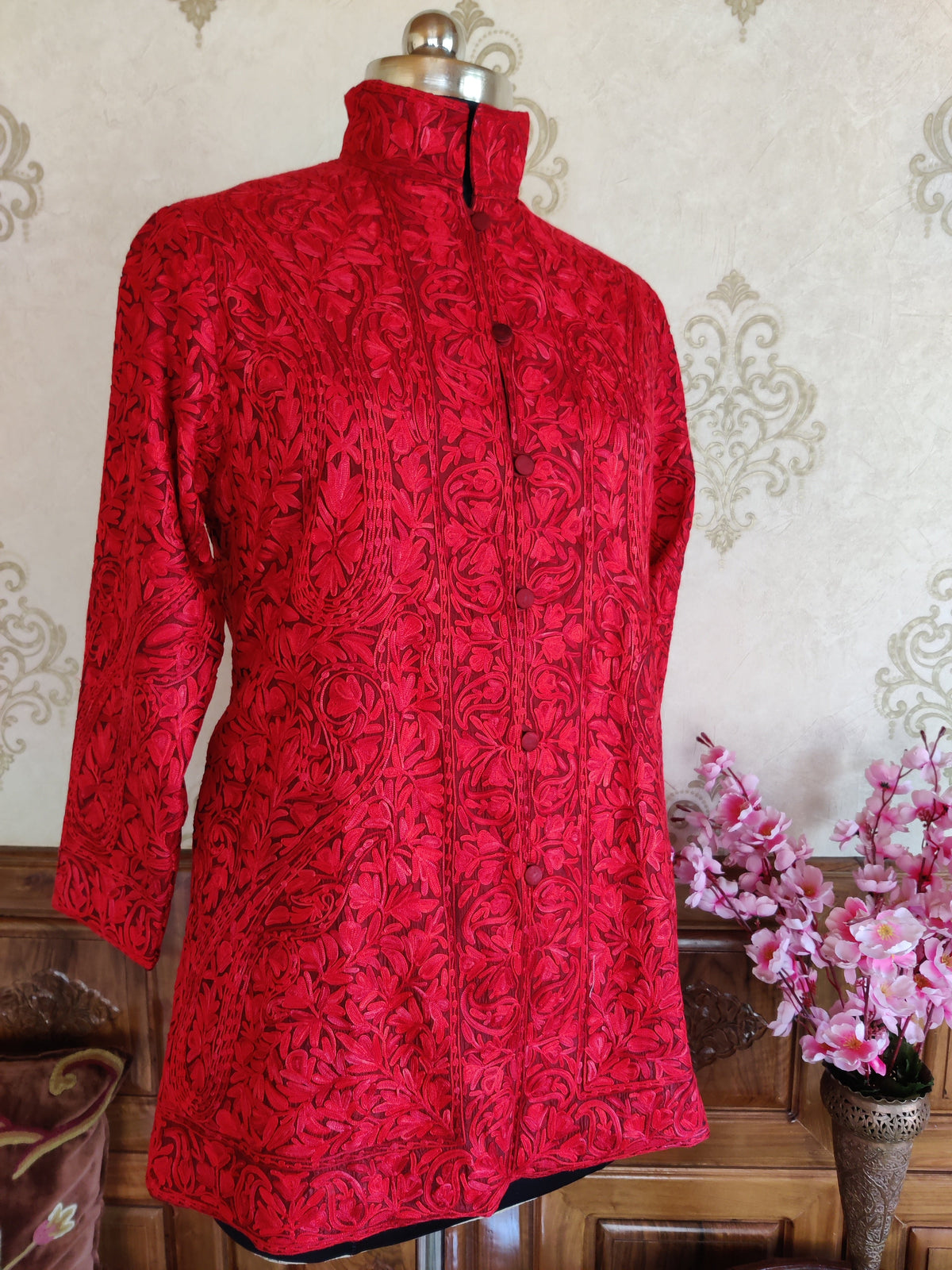 Front view of red coat with sleeves hanging, showing dense tonal Aari paisleys and floral borders