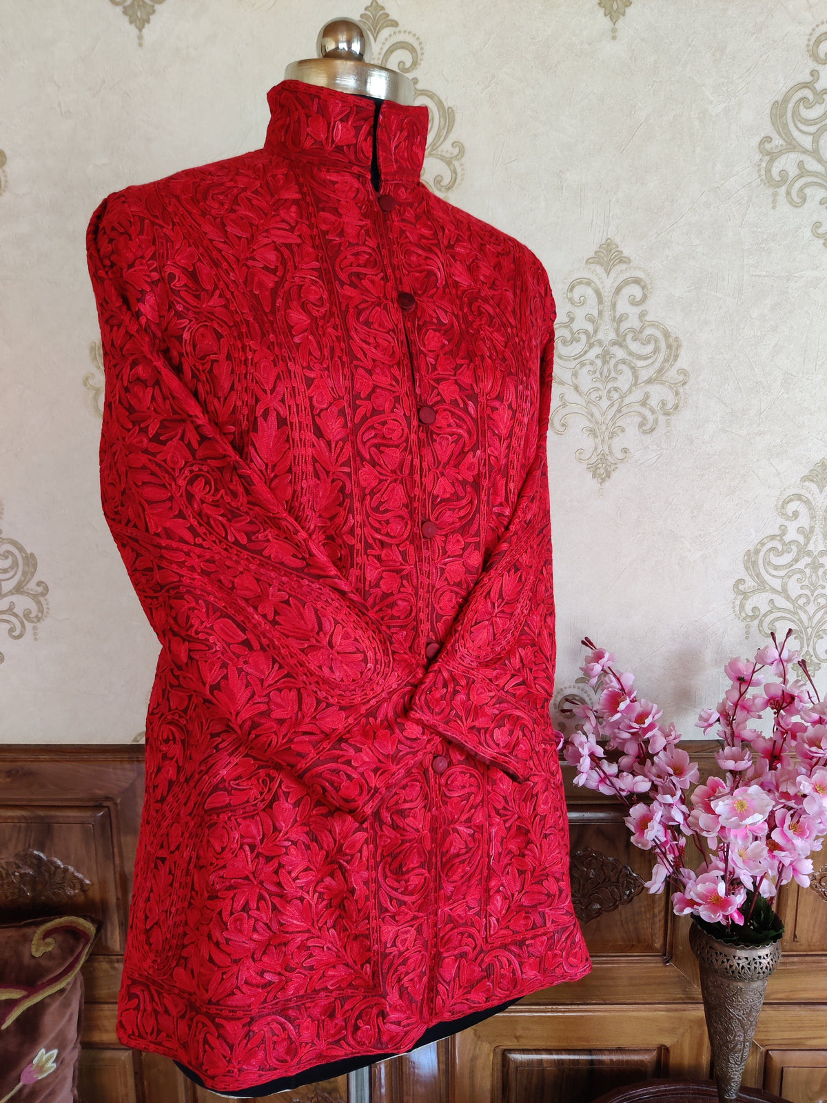 Front view of red coat with sleeves crossed, standing collar and dense tonal Aari floral and paisley embroidery