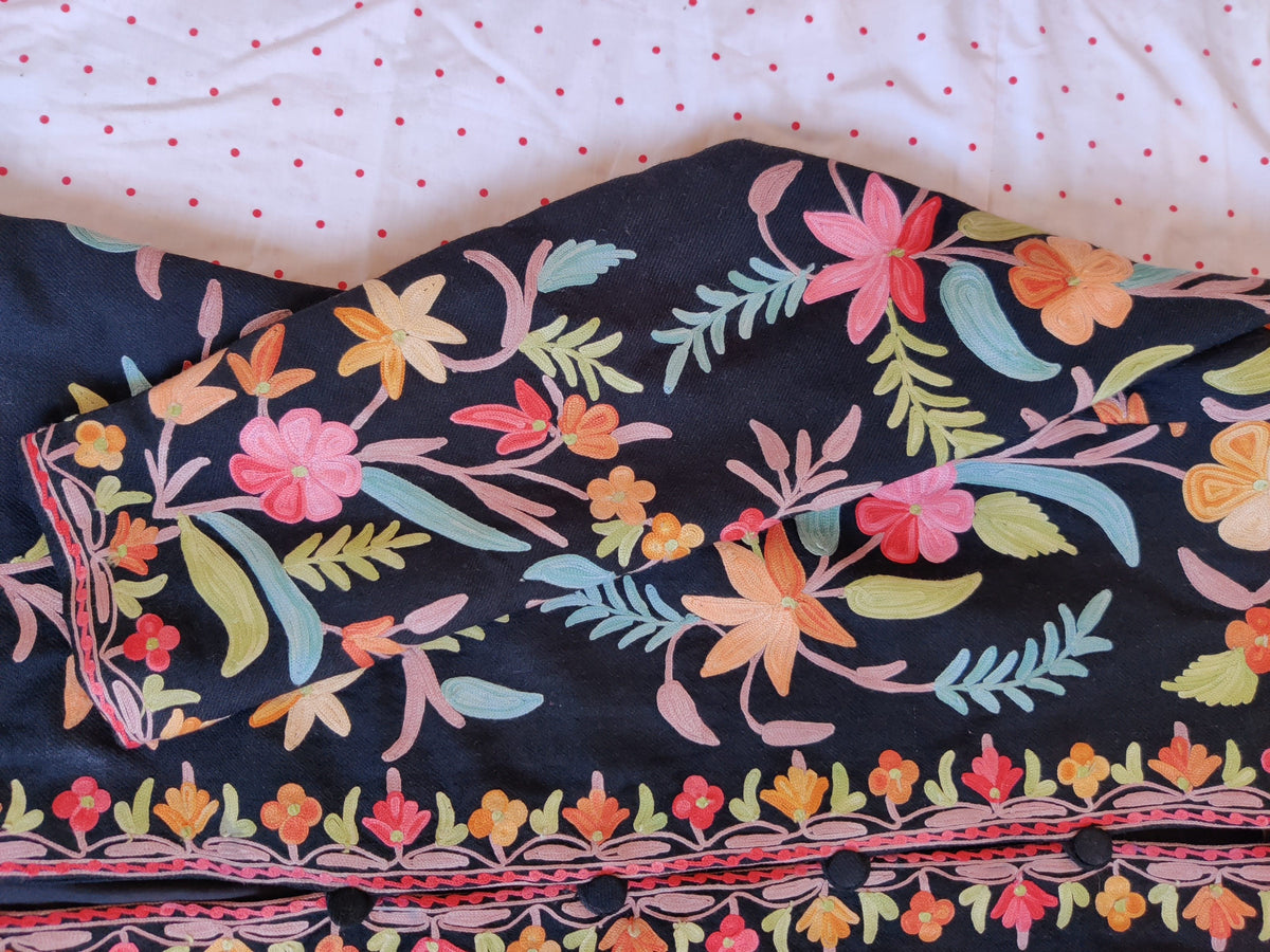 Close-up of a folded sleeve and front border on black jacket, with colourful Aari flowers and pale blue and green leaves