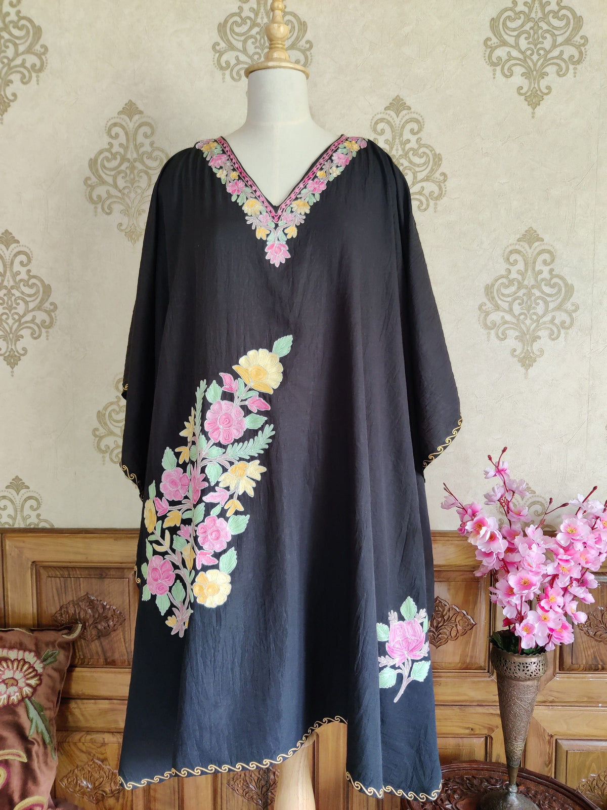 Full front of a black kaftan with a pastel floral V-neck, a large pink and yellow Aari flower spray and a smaller motif near the hem
